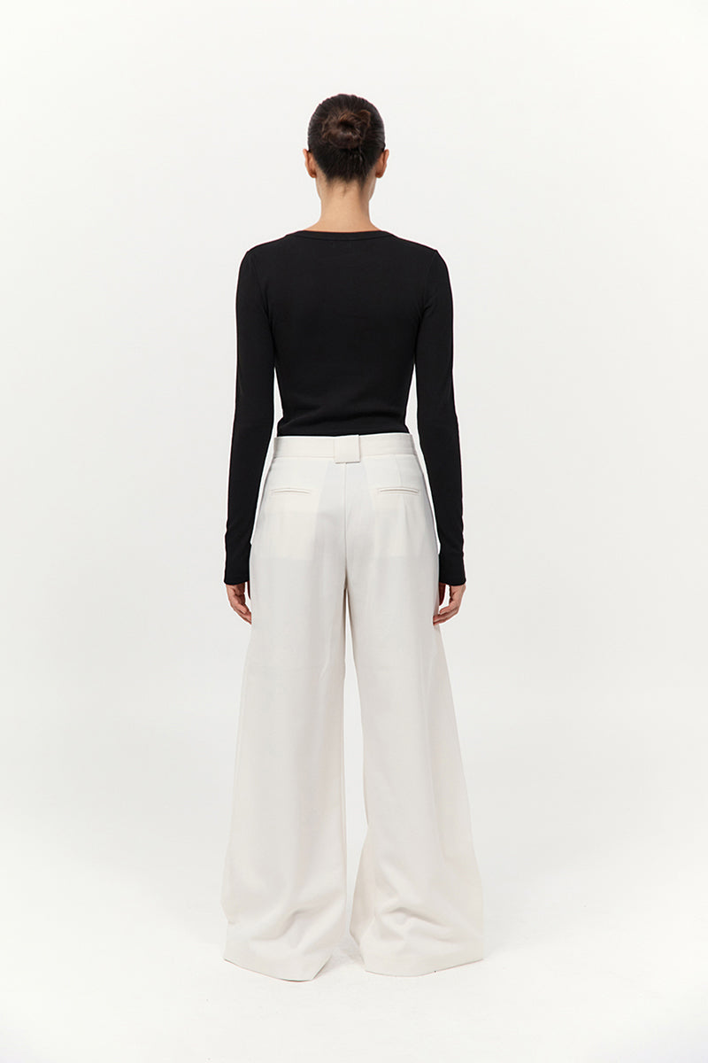 Person wearing a black long-sleeve top and white wide-leg pants on a white background