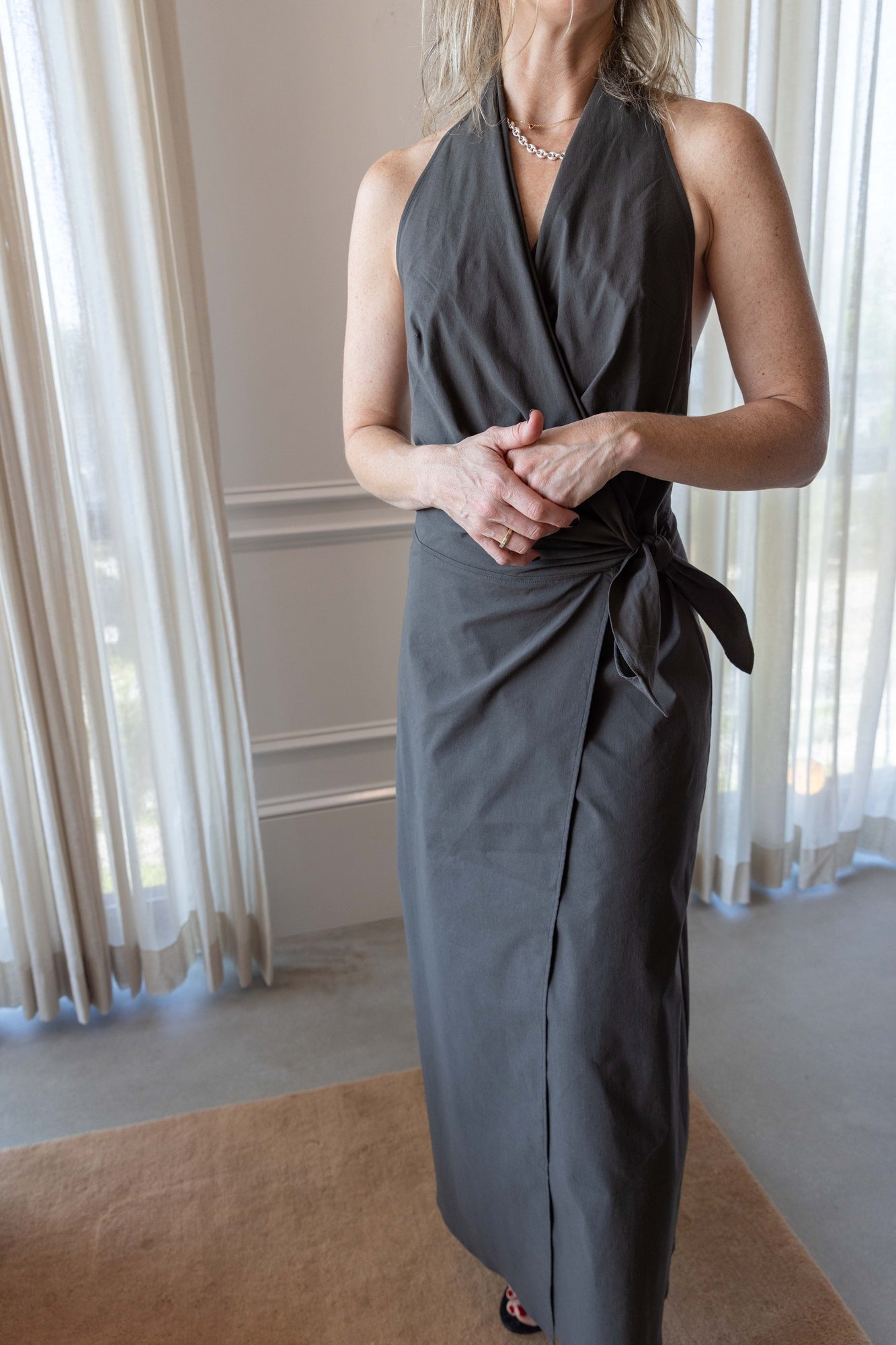 Woman wearing the St Agni Halter Wrap Backless Dress standing against white curtains