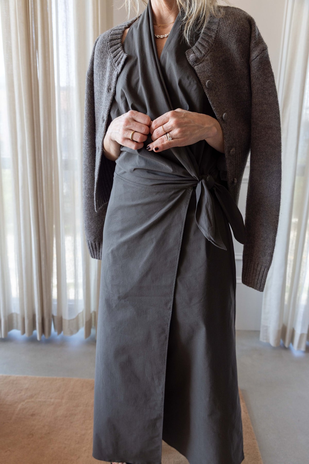 Woman wearing the St Agni Halter Wrap Backless Dress standing and wool cardigan against white curtains