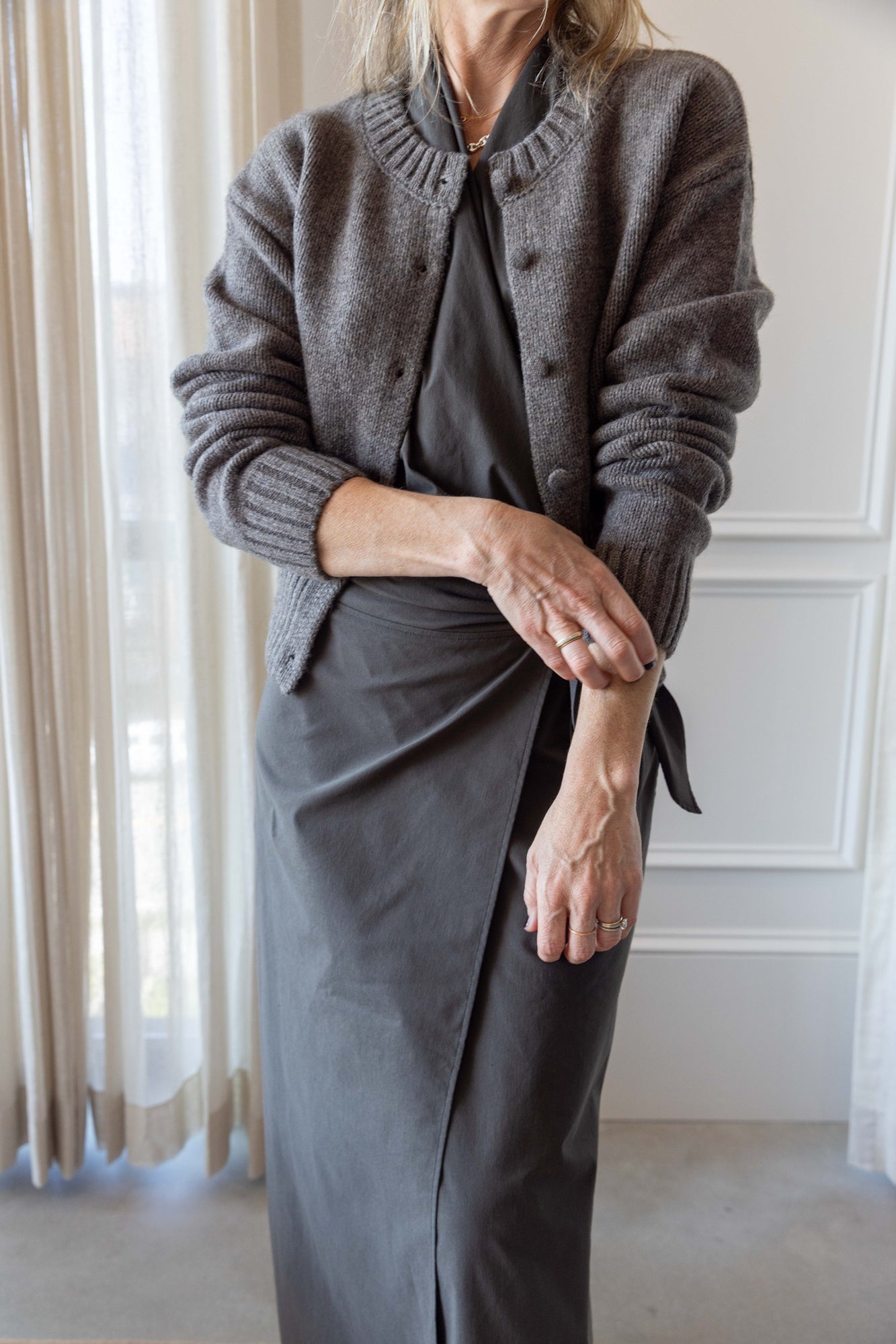 Woman wearing the St Agni Halter Wrap Backless Dress and wool sweater standing against white curtains