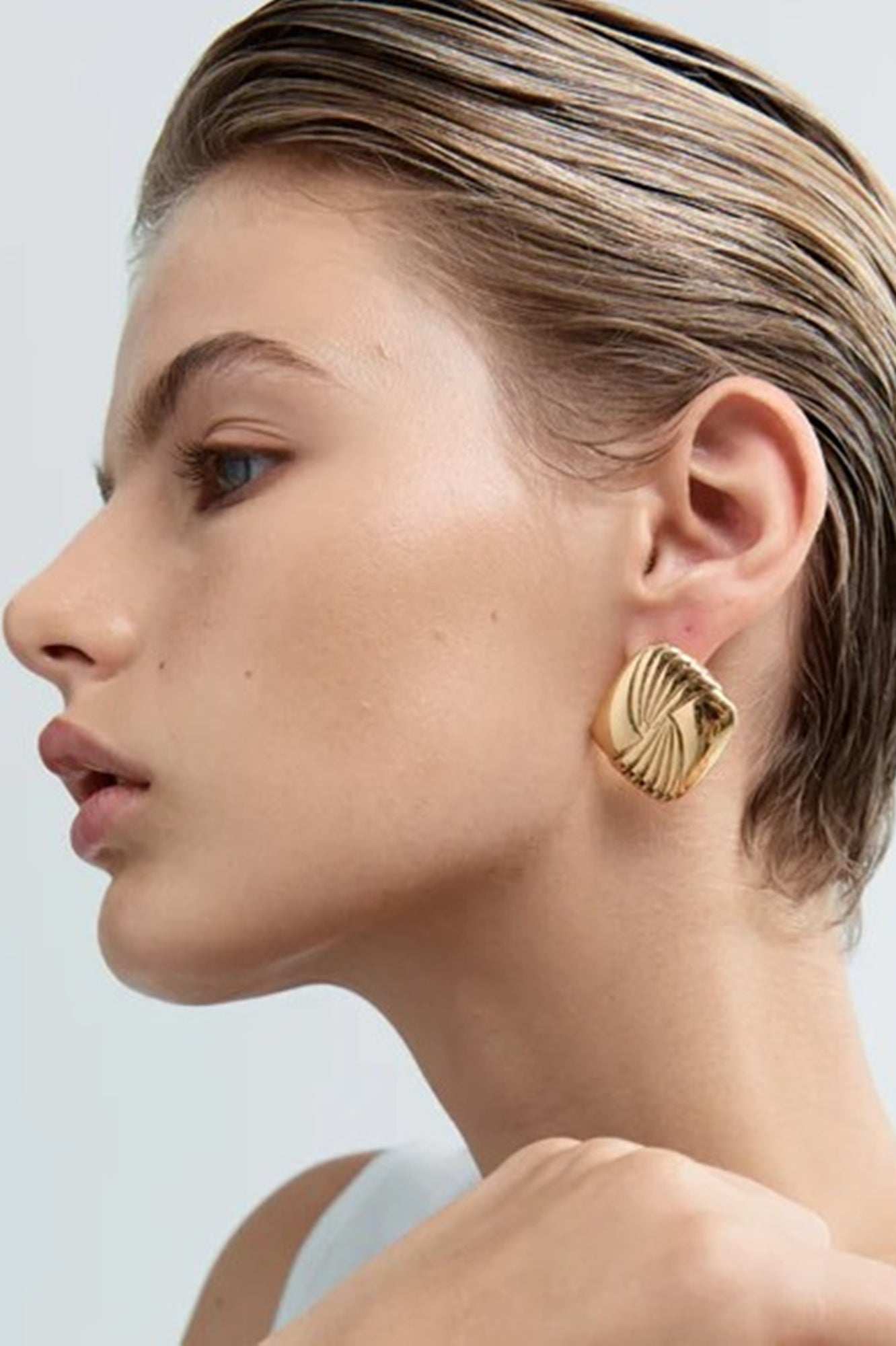 Close-up of a woman wearing gold earrings against a neutral background