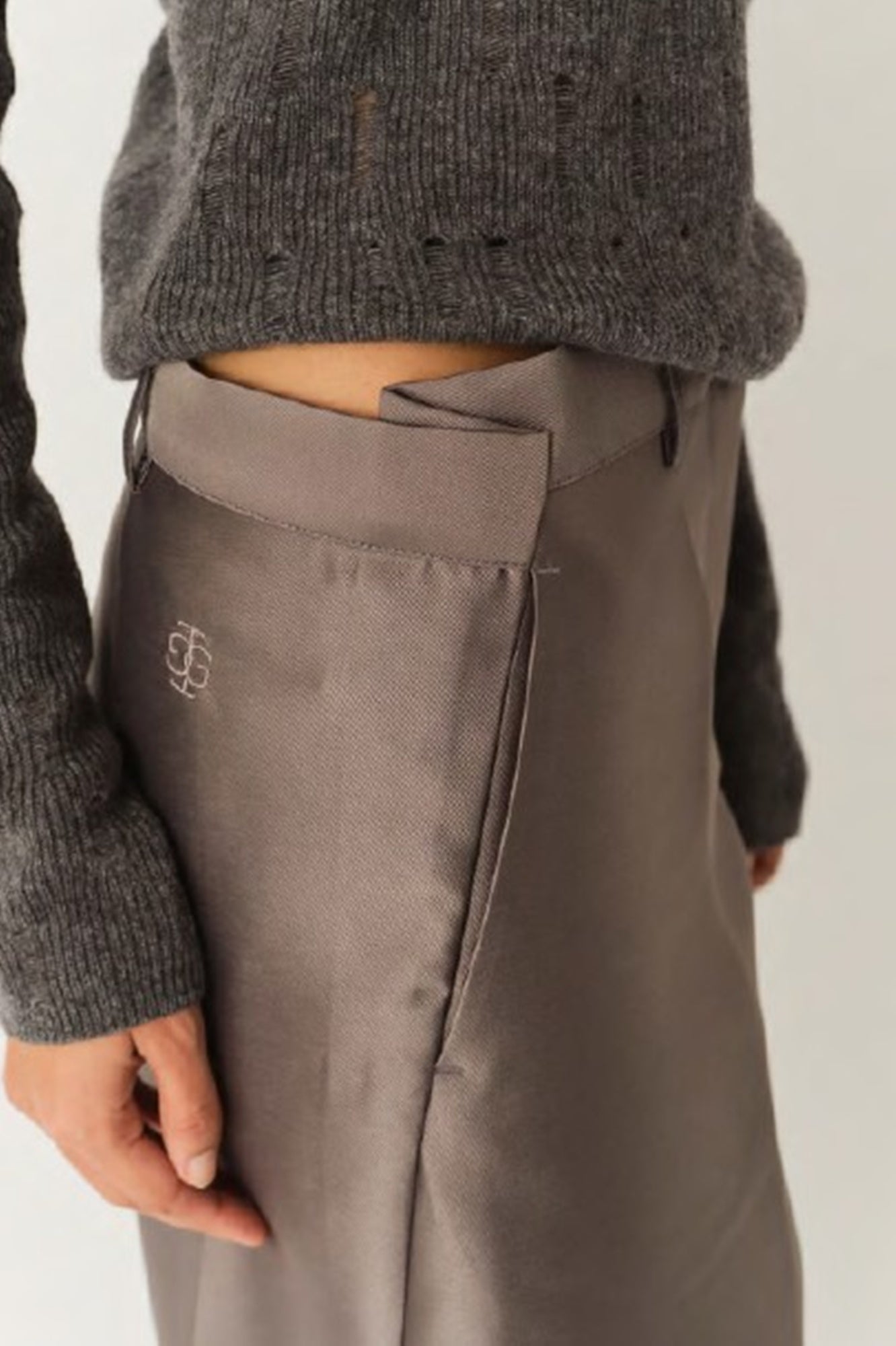 Person wearing gray pants with a brand logo on a plain background