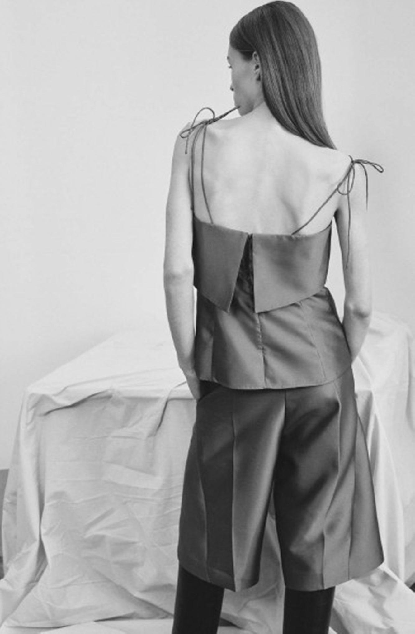 Woman wearing a backless dress with ribbon straps on a plain background