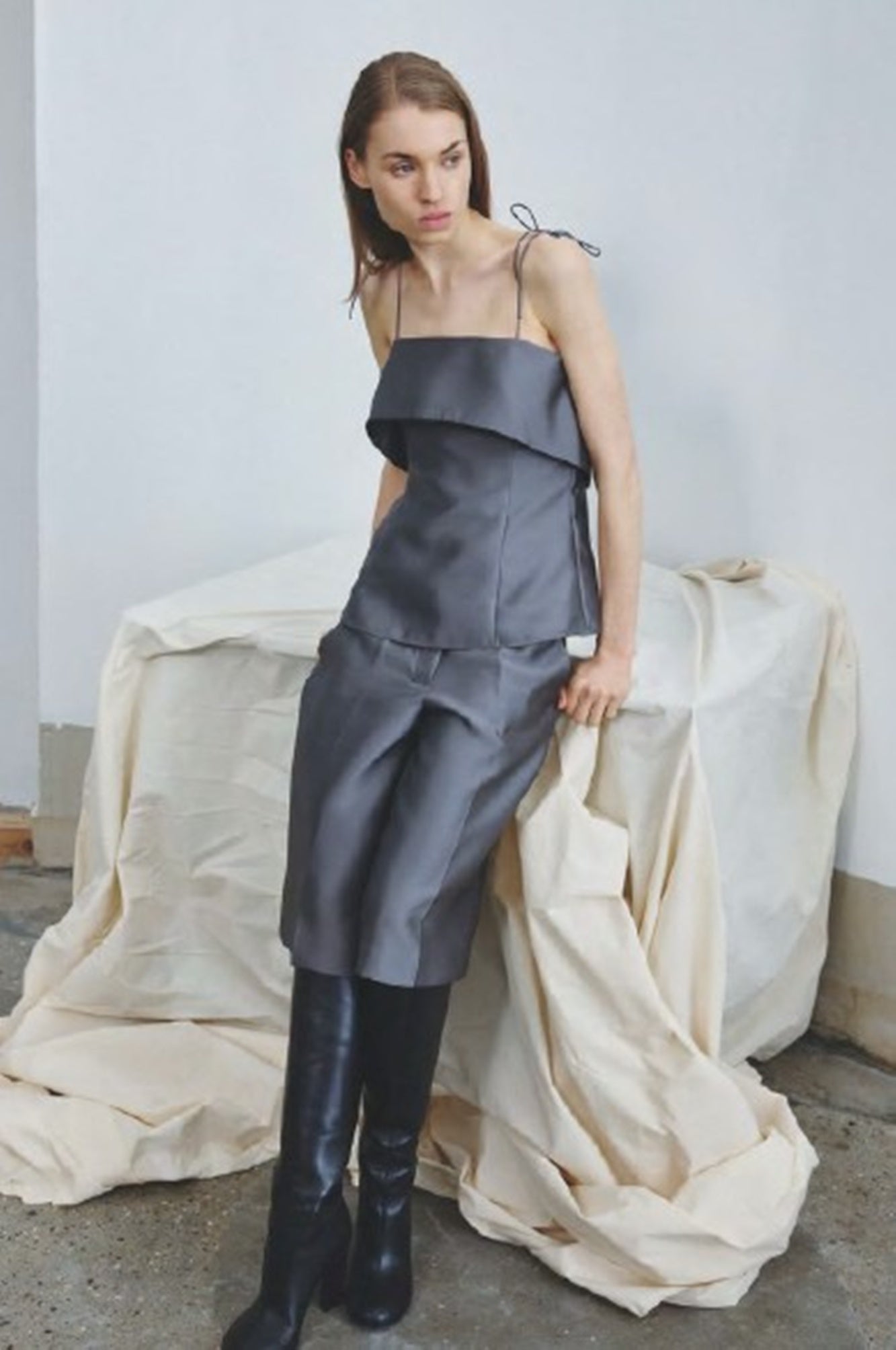 Woman wearing a gray outfit with black boots in a minimalistic setting