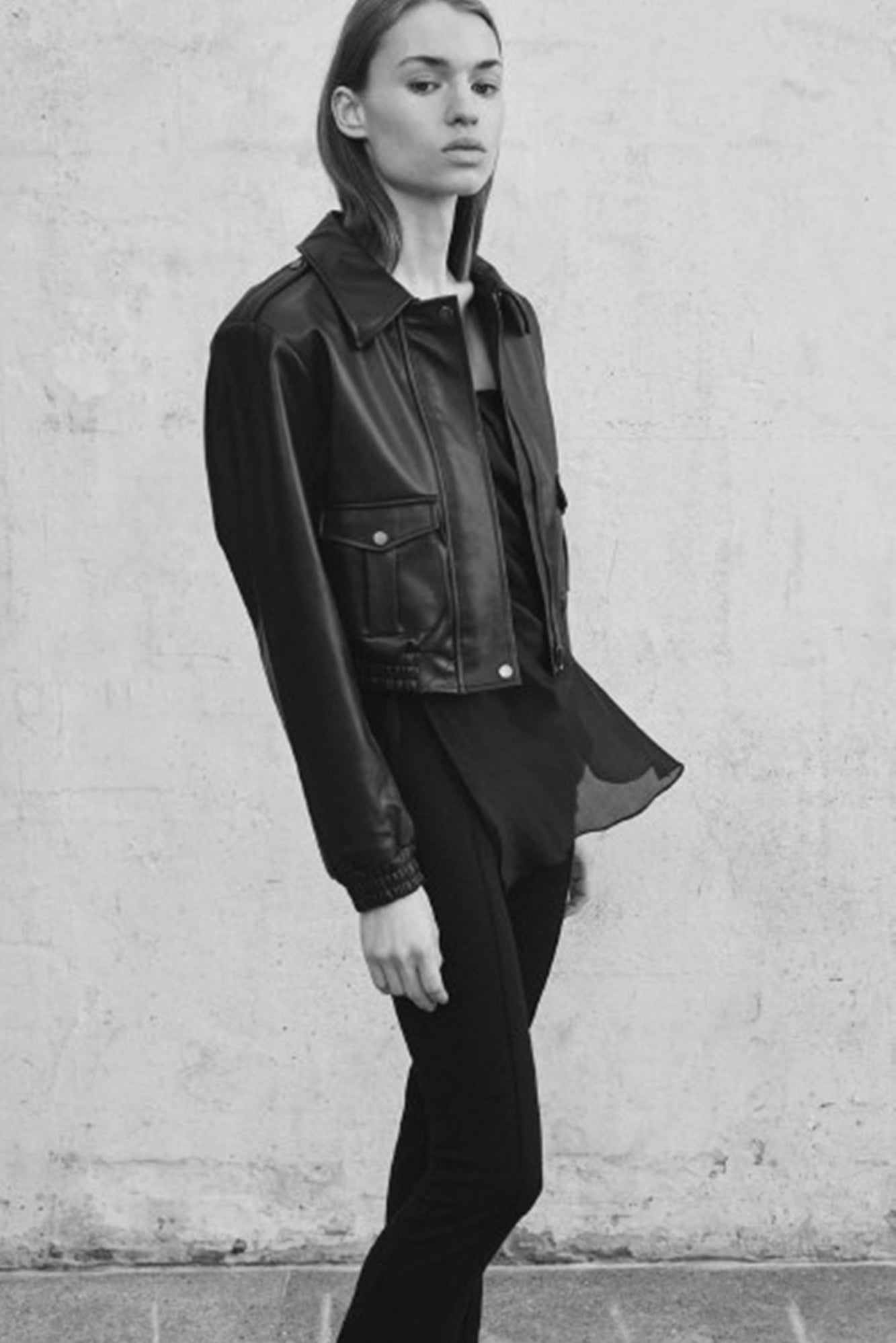 Person wearing a black leather jacket and outfit against a light-colored wall.