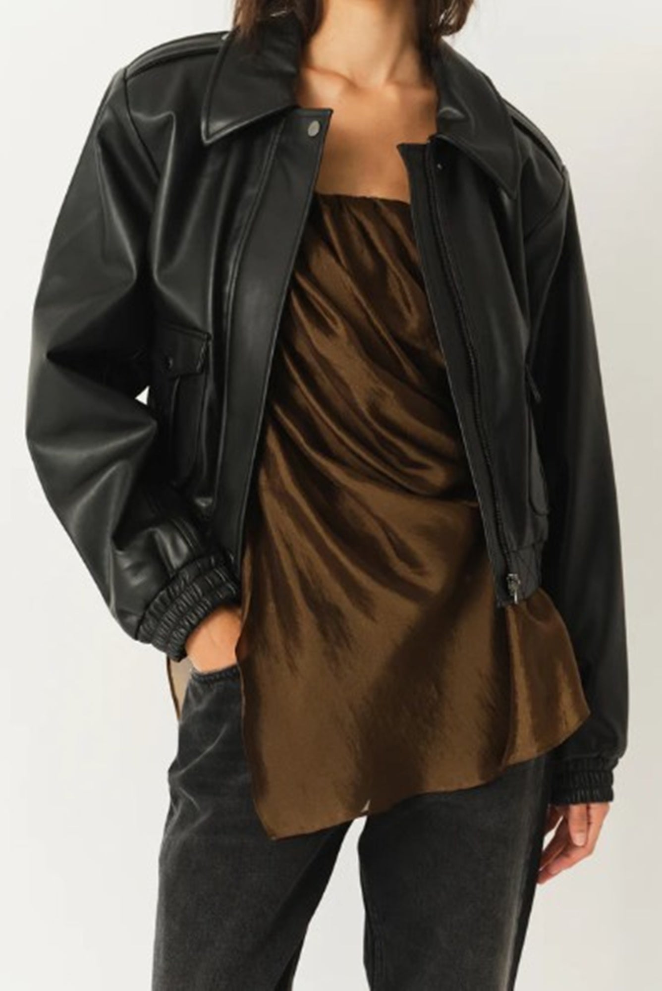 Person wearing a black leather jacket over a brown top on a white background