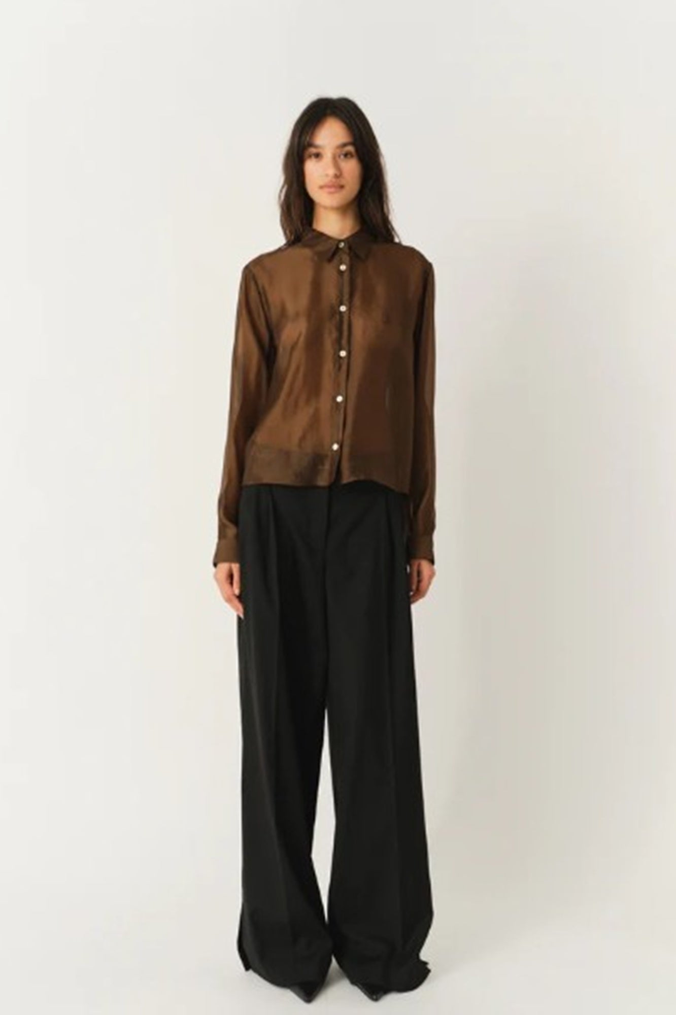 Person wearing a brown shirt and black pants on a white background