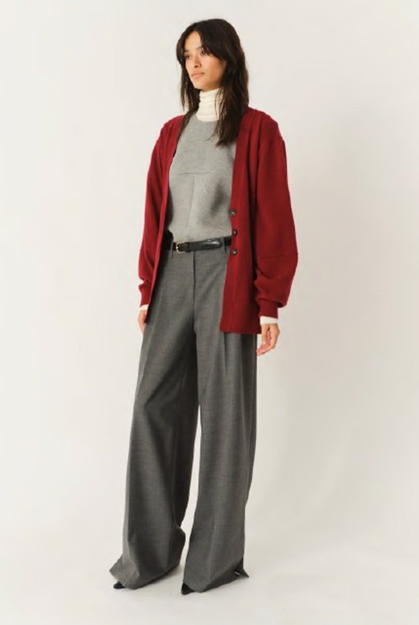 Woman wearing a red cardigan, gray turtleneck, and wide-leg pants on a white background