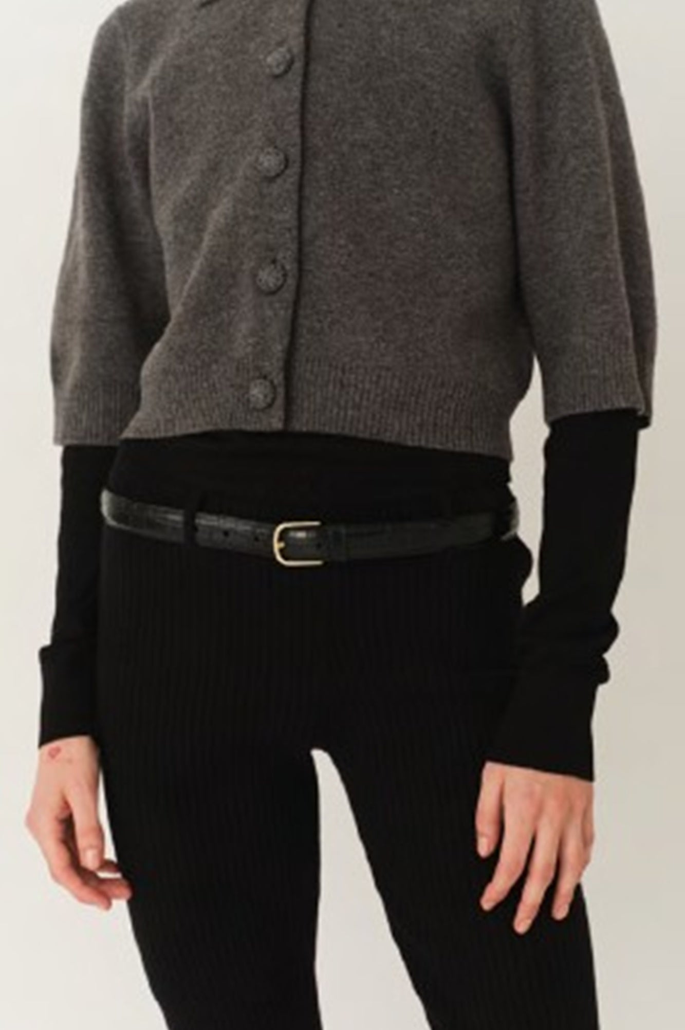 Person wearing a gray cardigan over a black long-sleeve shirt and pants on a white background