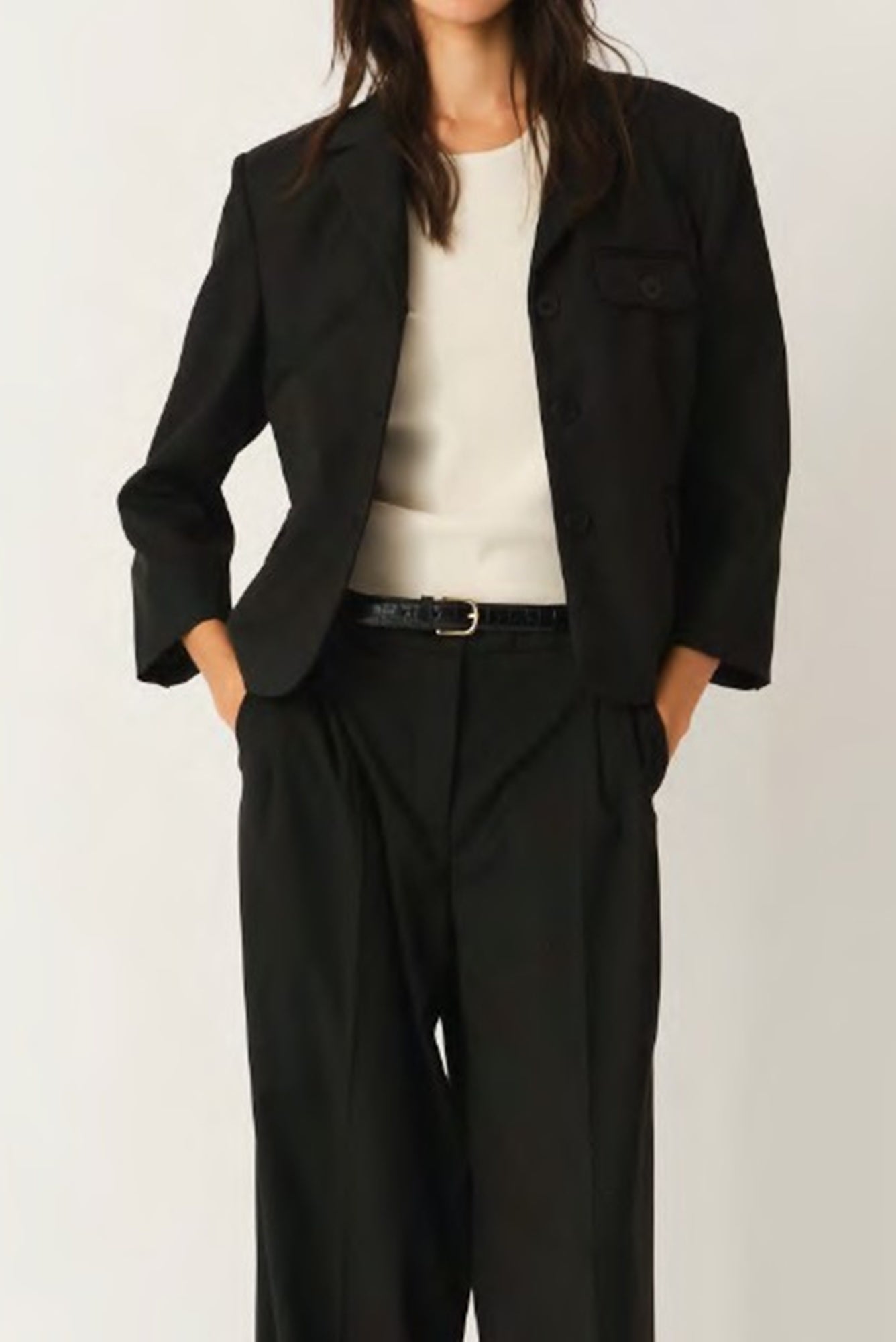 Person wearing a black suit with a white shirt on a plain background