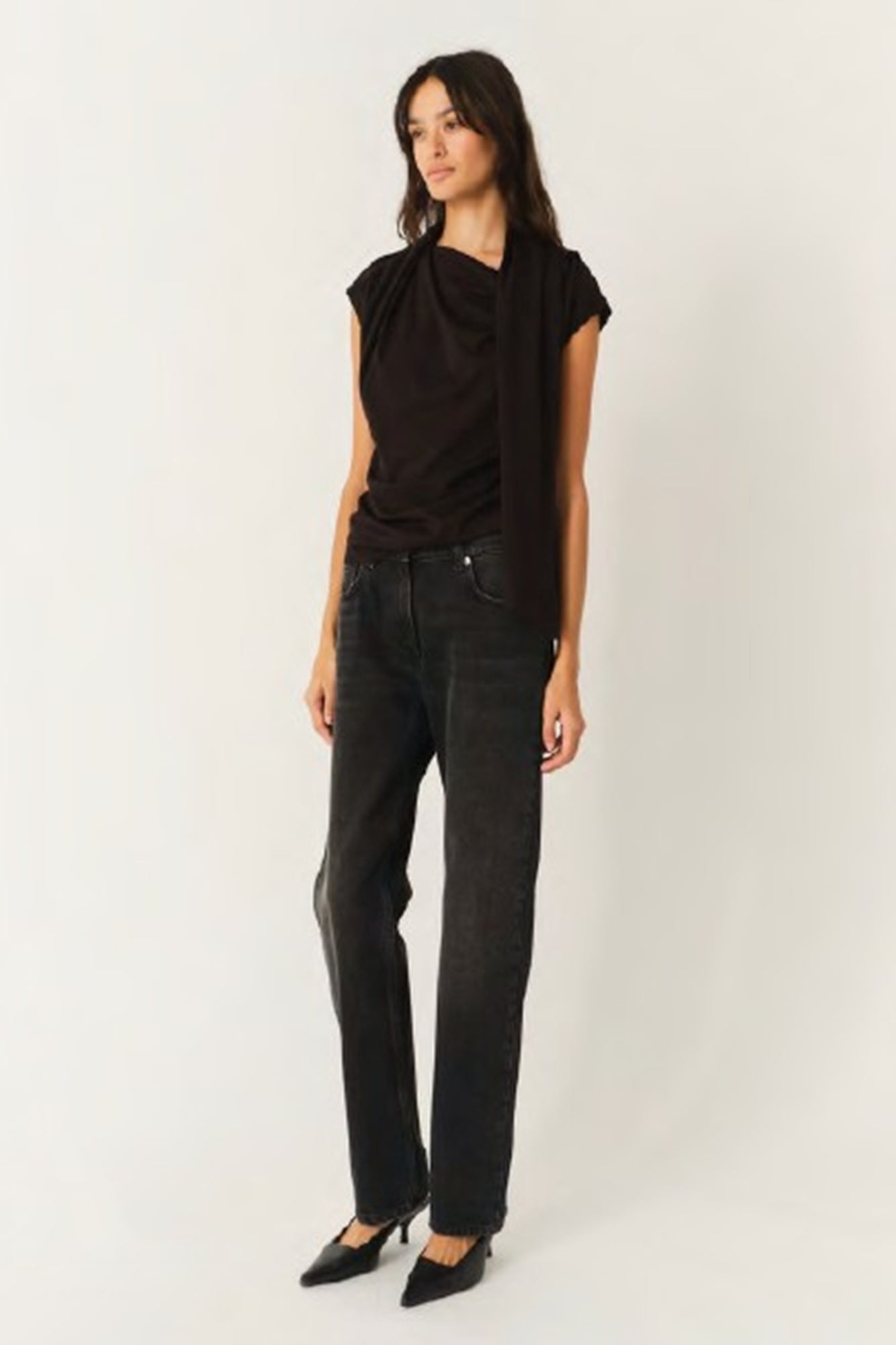 Woman wearing a black top and dark jeans on a white background