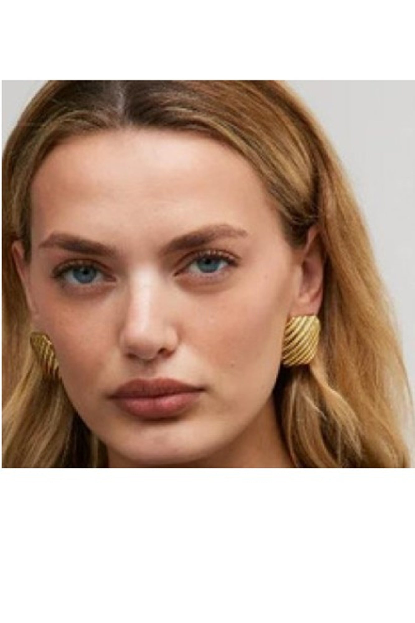 Close-up of a woman wearing gold hoop earrings with a plain background