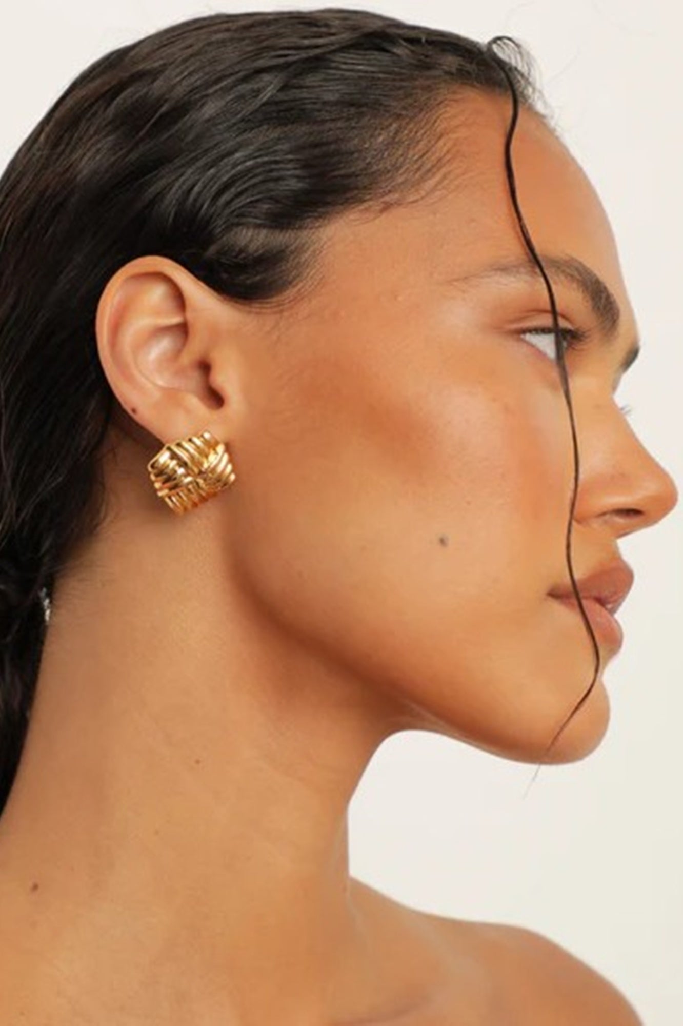 Close-up of a person wearing gold hoop earrings on a plain background