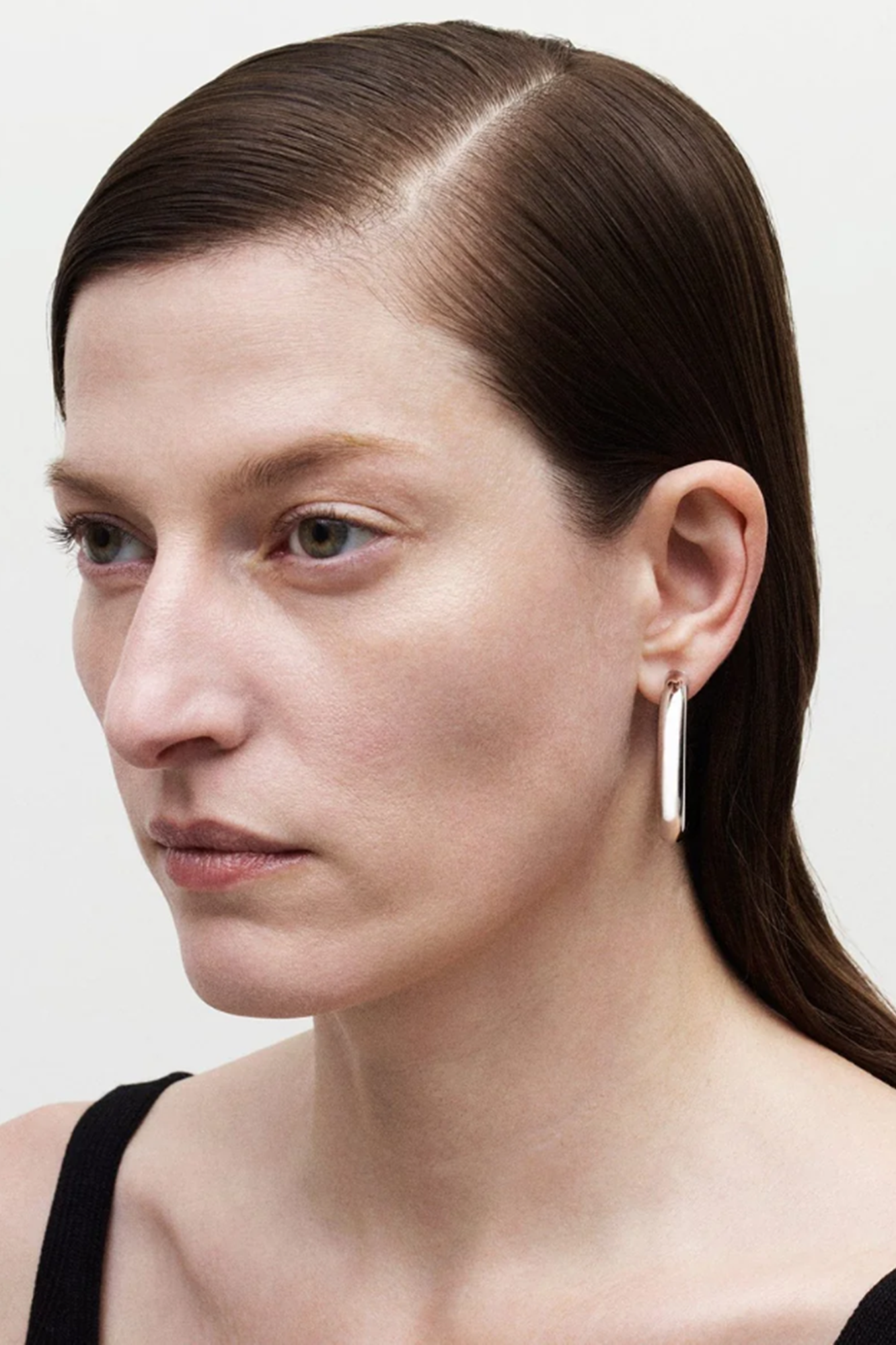 Close-up of a woman wearing a gold earring against a plain background