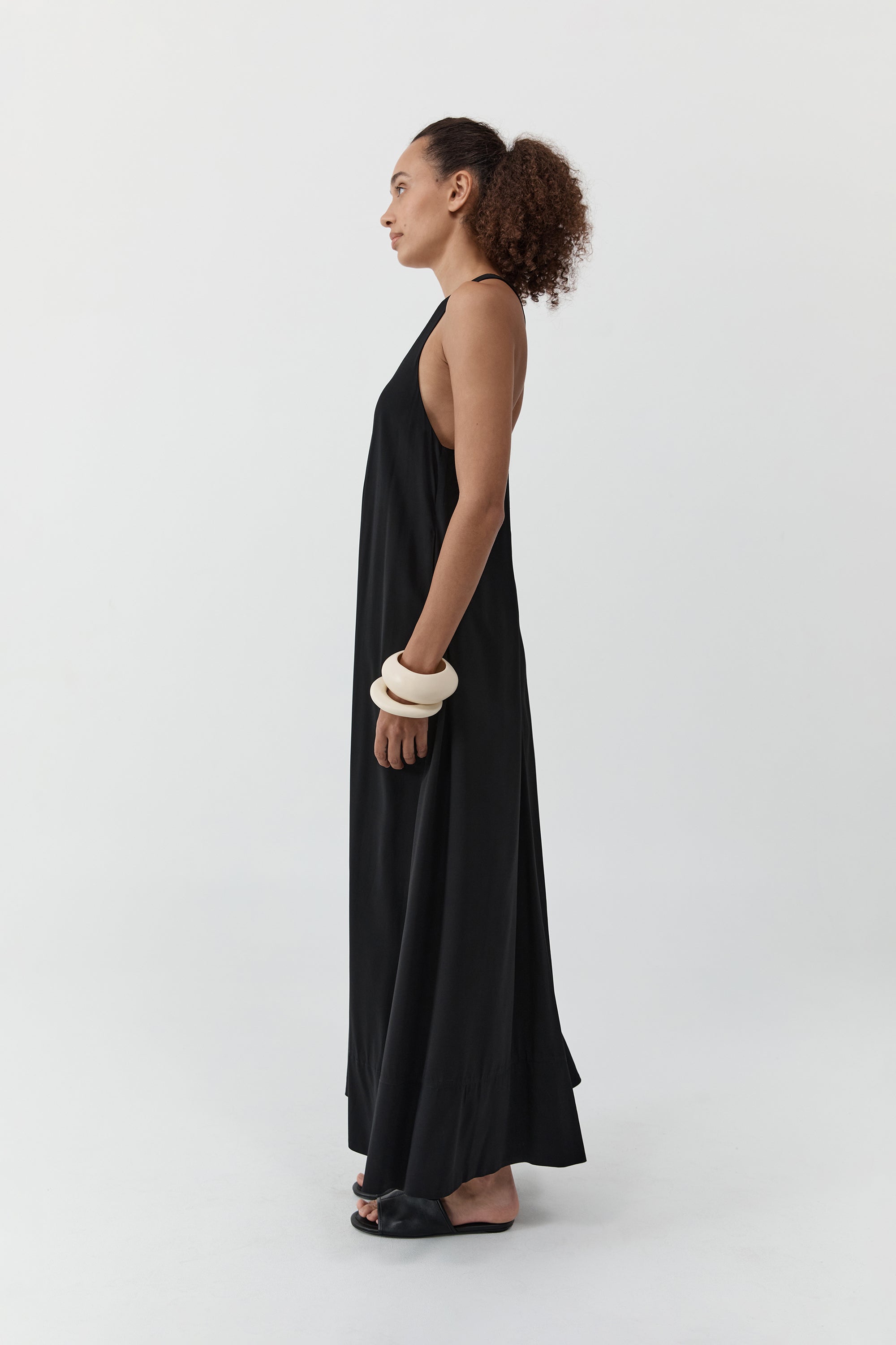 Side profile of a woman wearing the st. agni fluid tank dress standing in front of a cream background