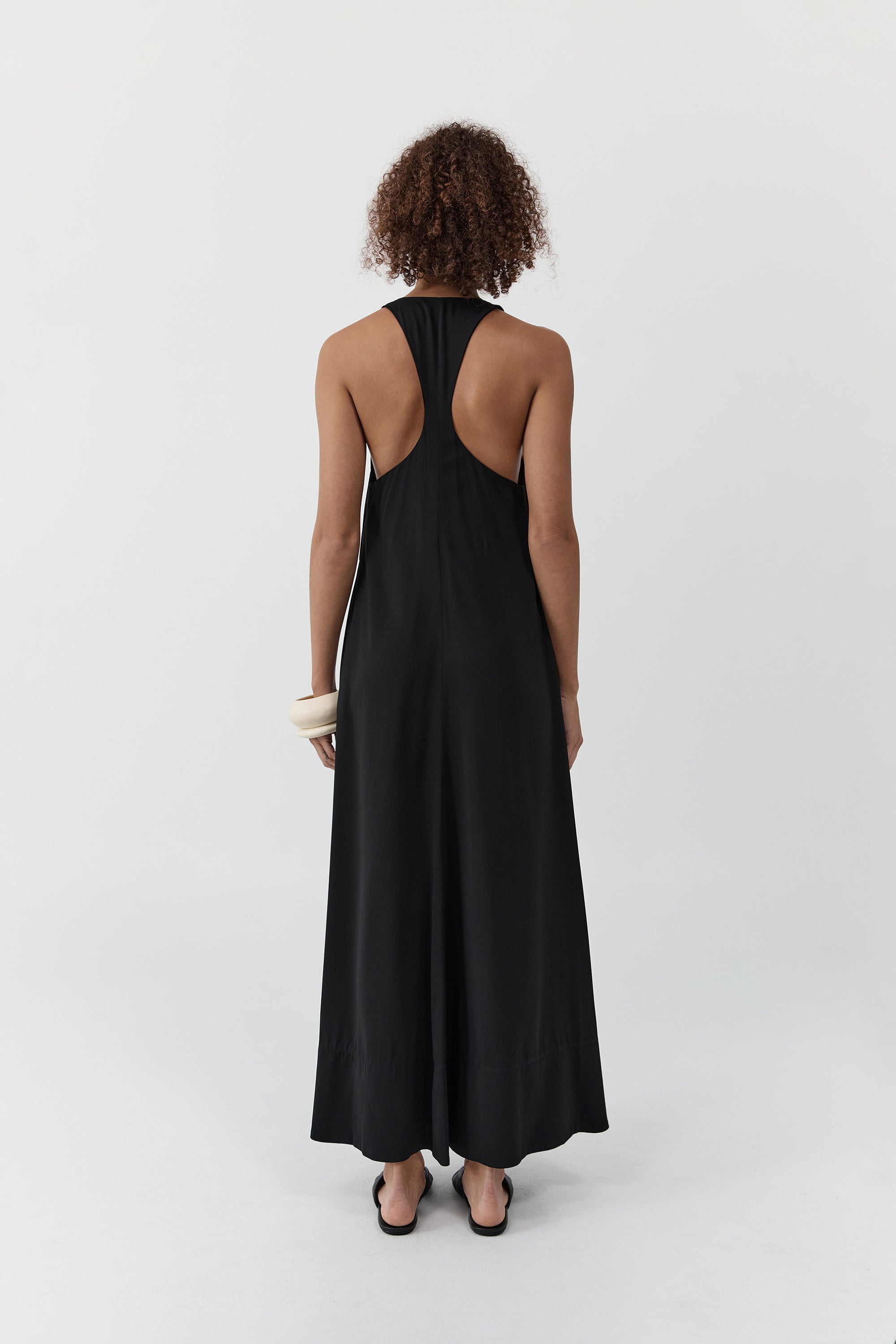 Backside of a woman wearing the st. agni fluid tank dress standing in front of a cream background