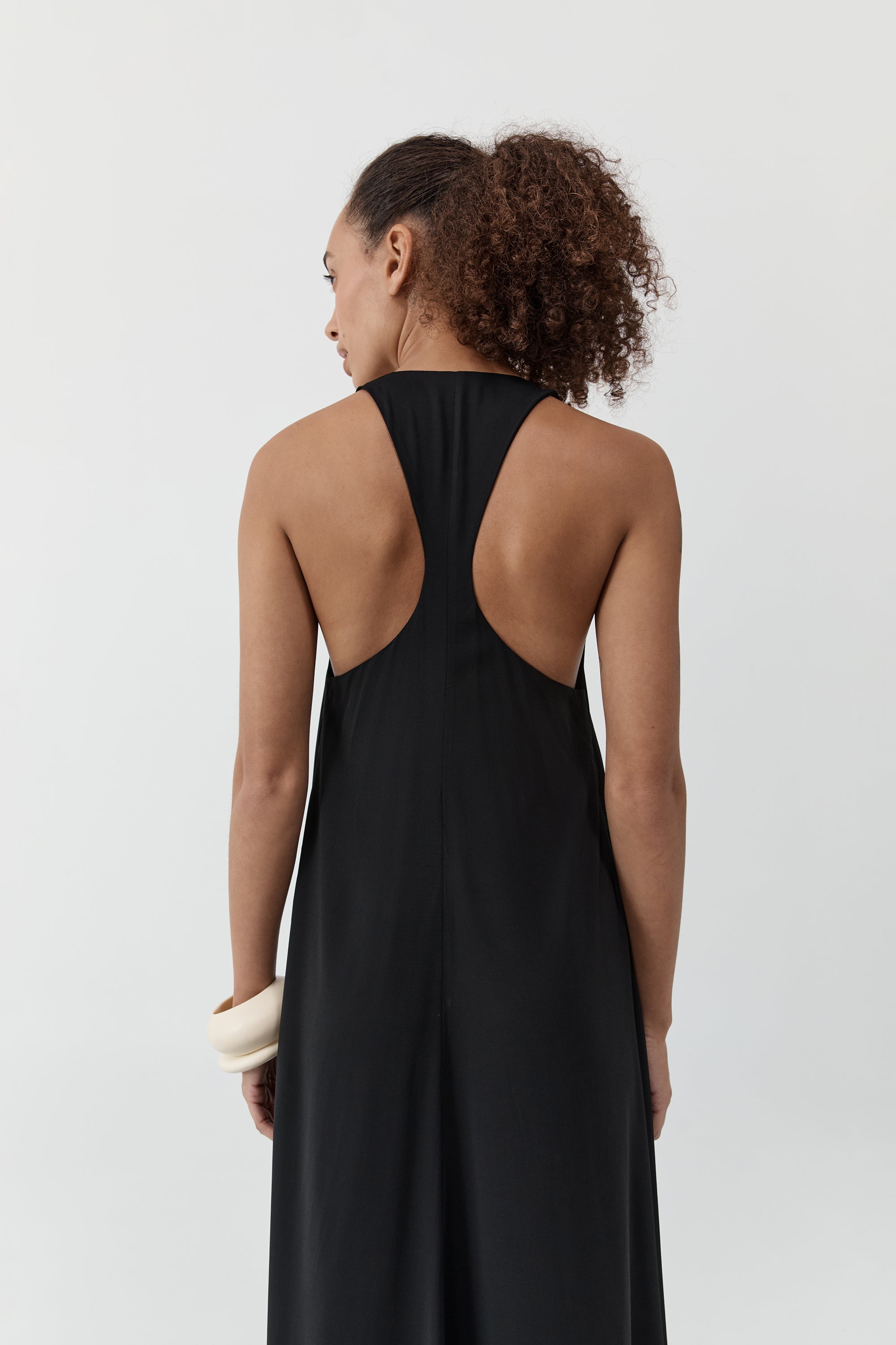 Backside of a woman wearing the st. agni fluid tank dress standing in front of a cream background