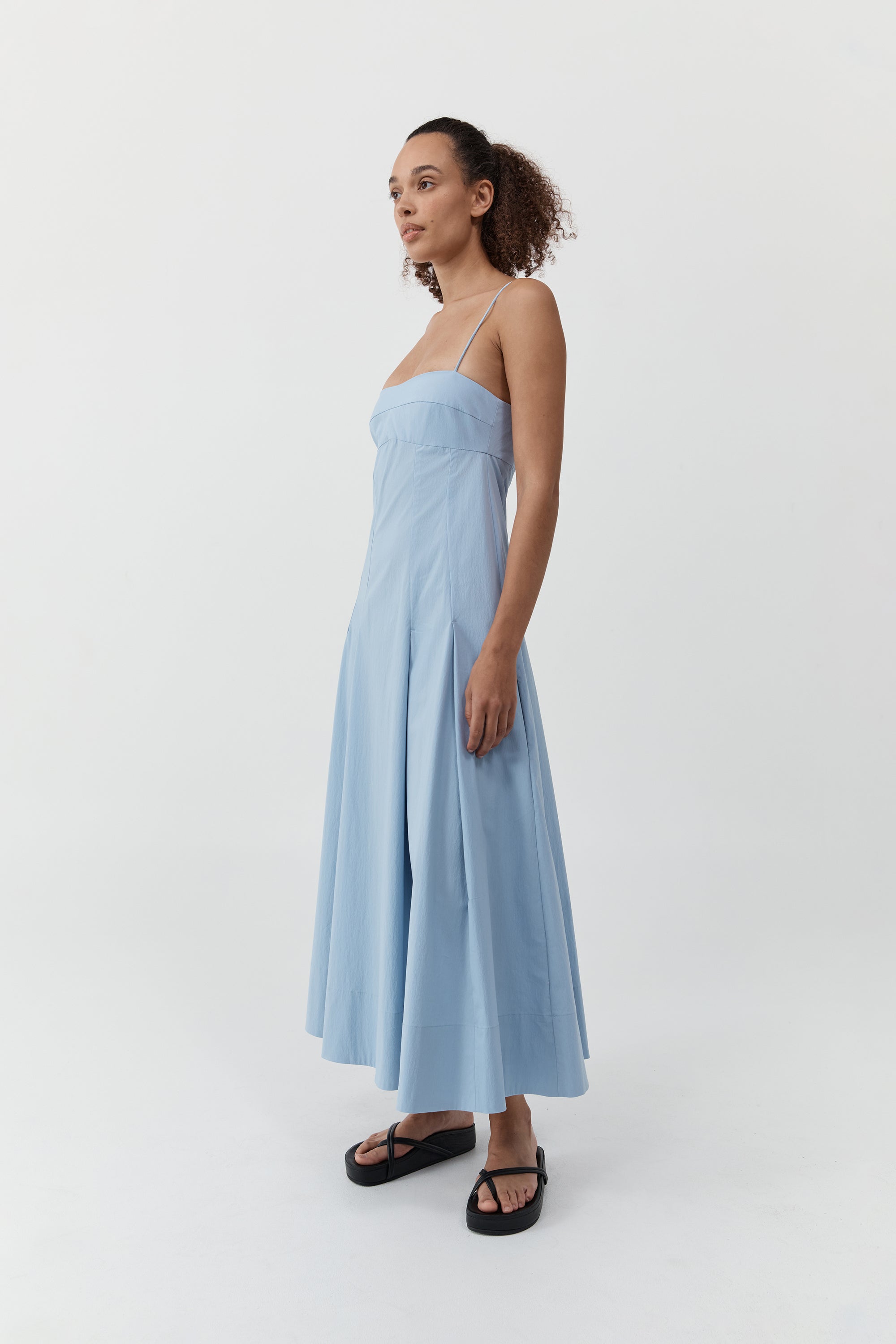 Woman wearing the st. agni everyday cotton pleated dress in sky in front of a cream background