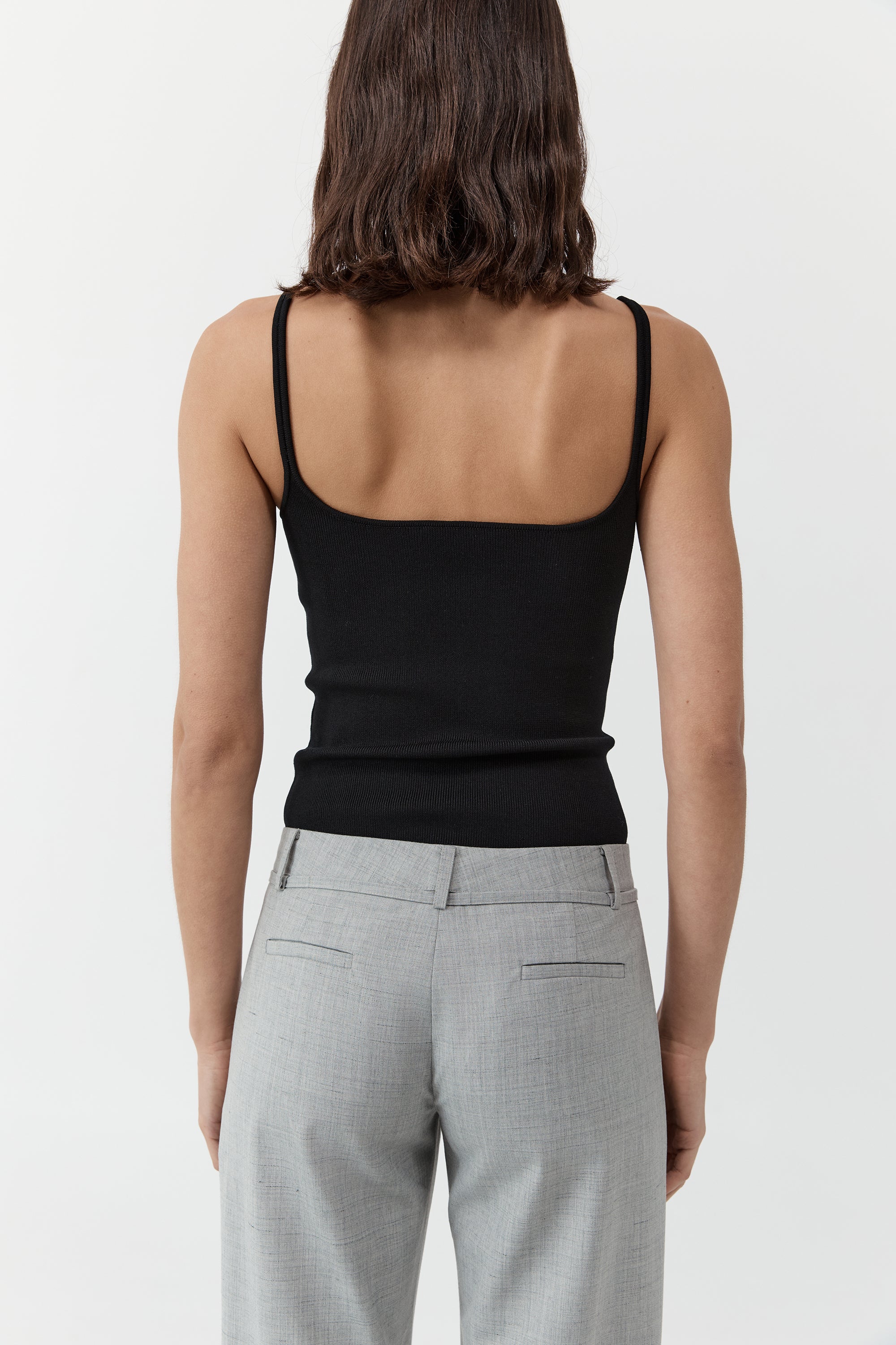 Backside of a woman wearing the st. agni slim square neck top In black with gray trousers in front of a cream background