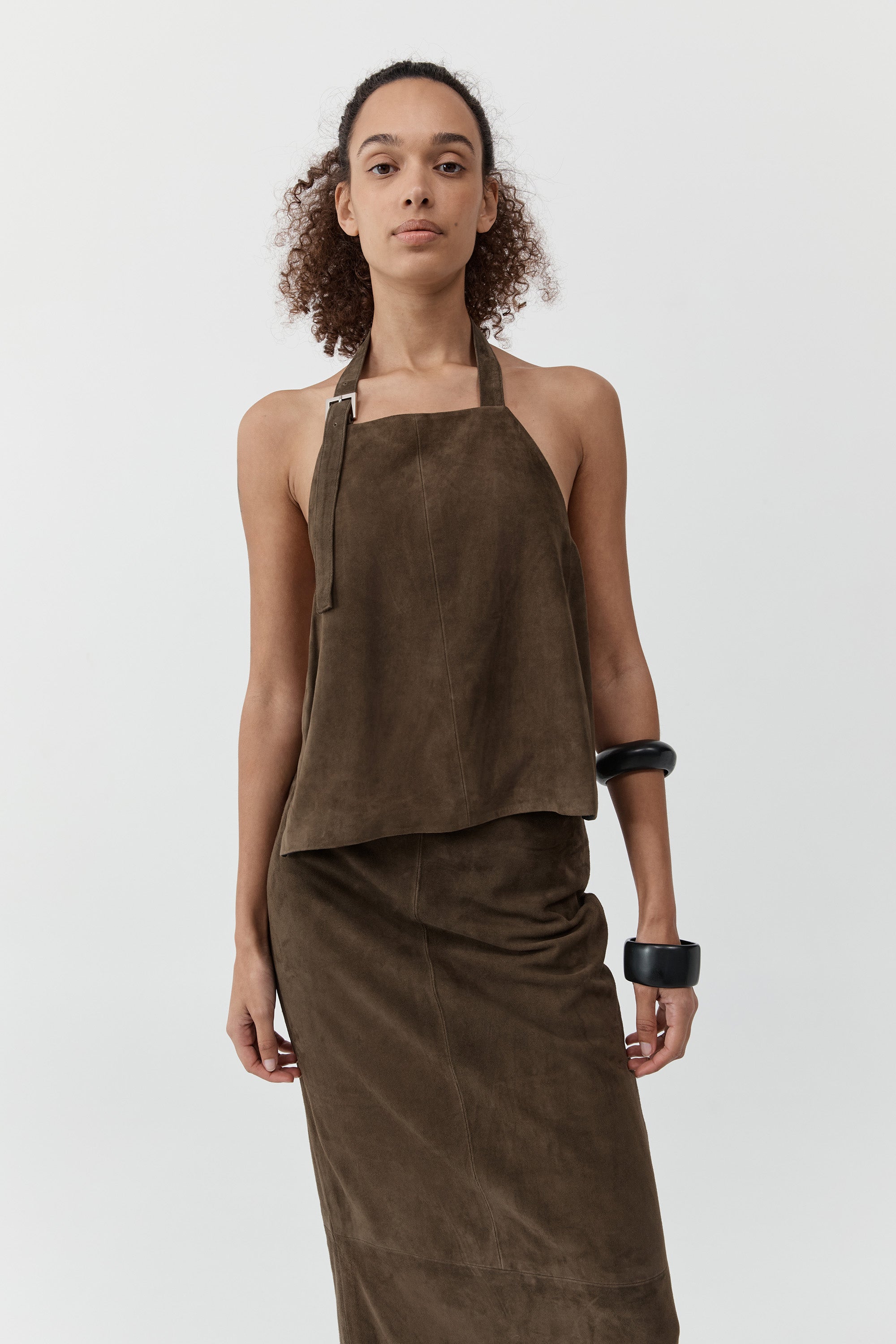 A woman wearing a st. agni suede apron top with suede skirt in front of a cream background