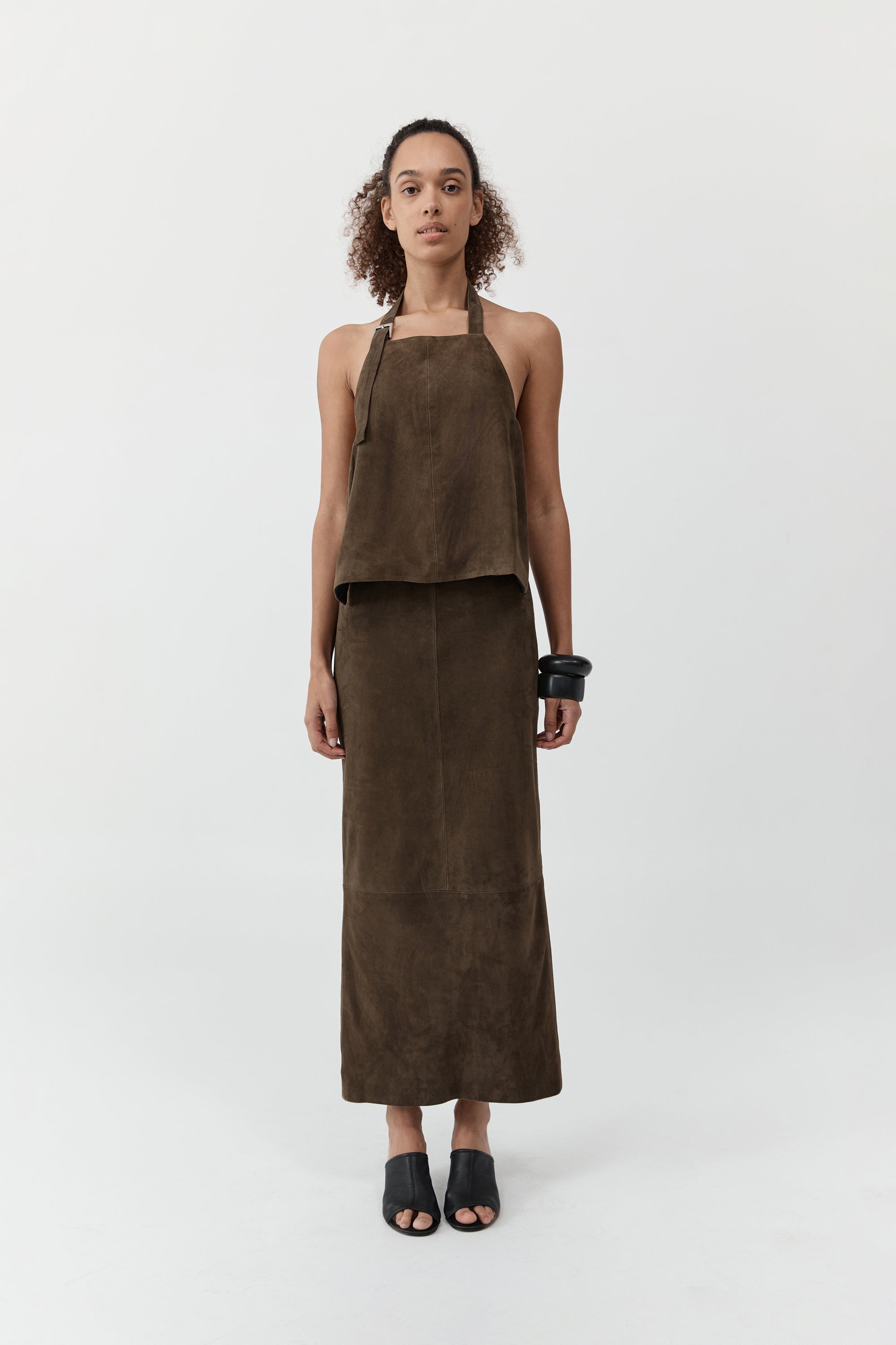 A woman wearing a st. agni suede apron top with suede skirt in front of a cream background