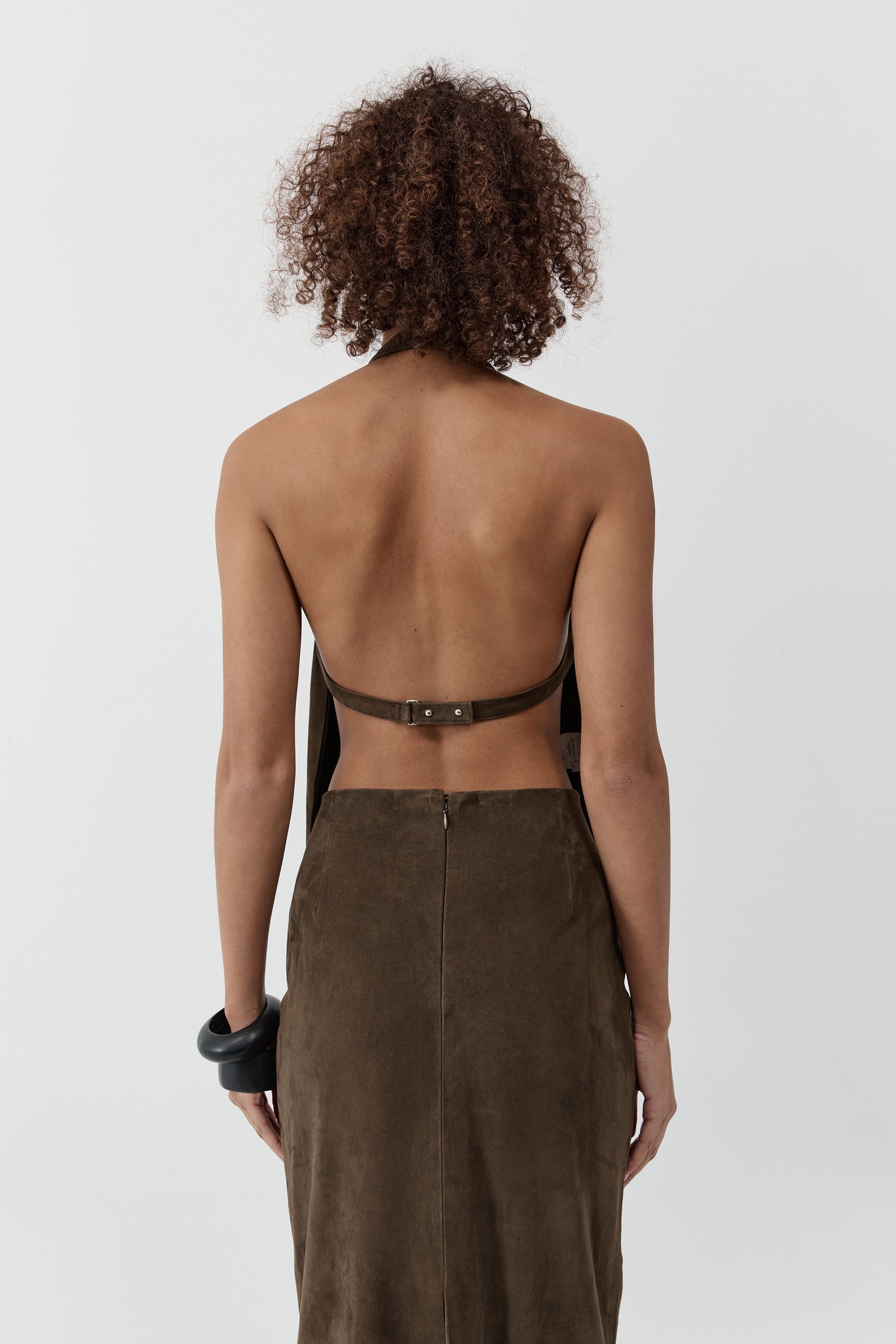 Close up backside of a woman wearing a st. agni suede apron top with suede skirt in front of a cream background