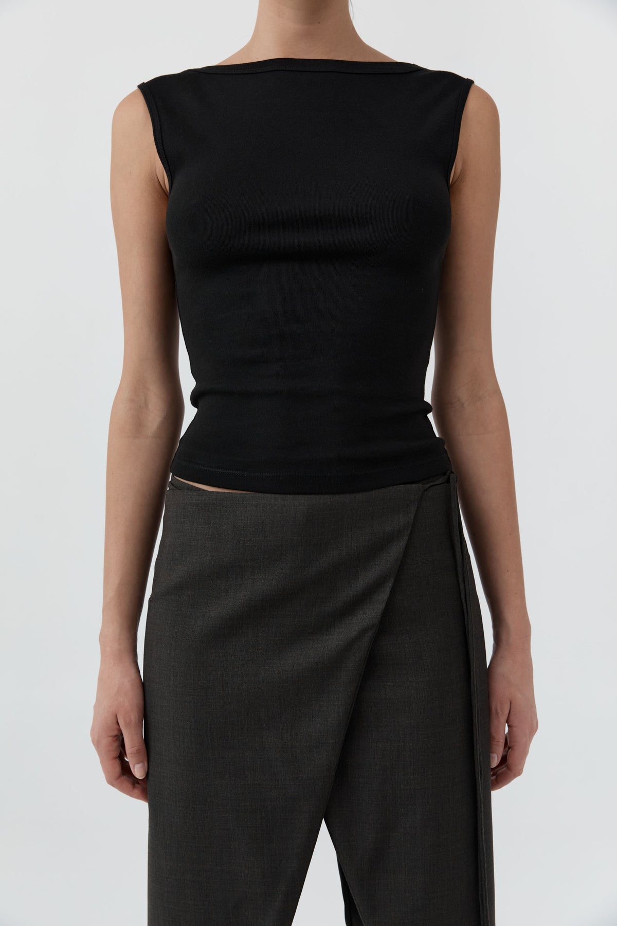 Close up of a woman wearing the St Agni Organic Cotton Ballerina Top-Jet Black with gray pants standing against a white background