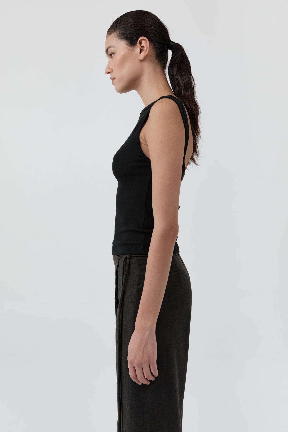 Side profile of a woman wearing the St Agni Organic Cotton Ballerina Top-Jet Black with gray pants standing against a white background