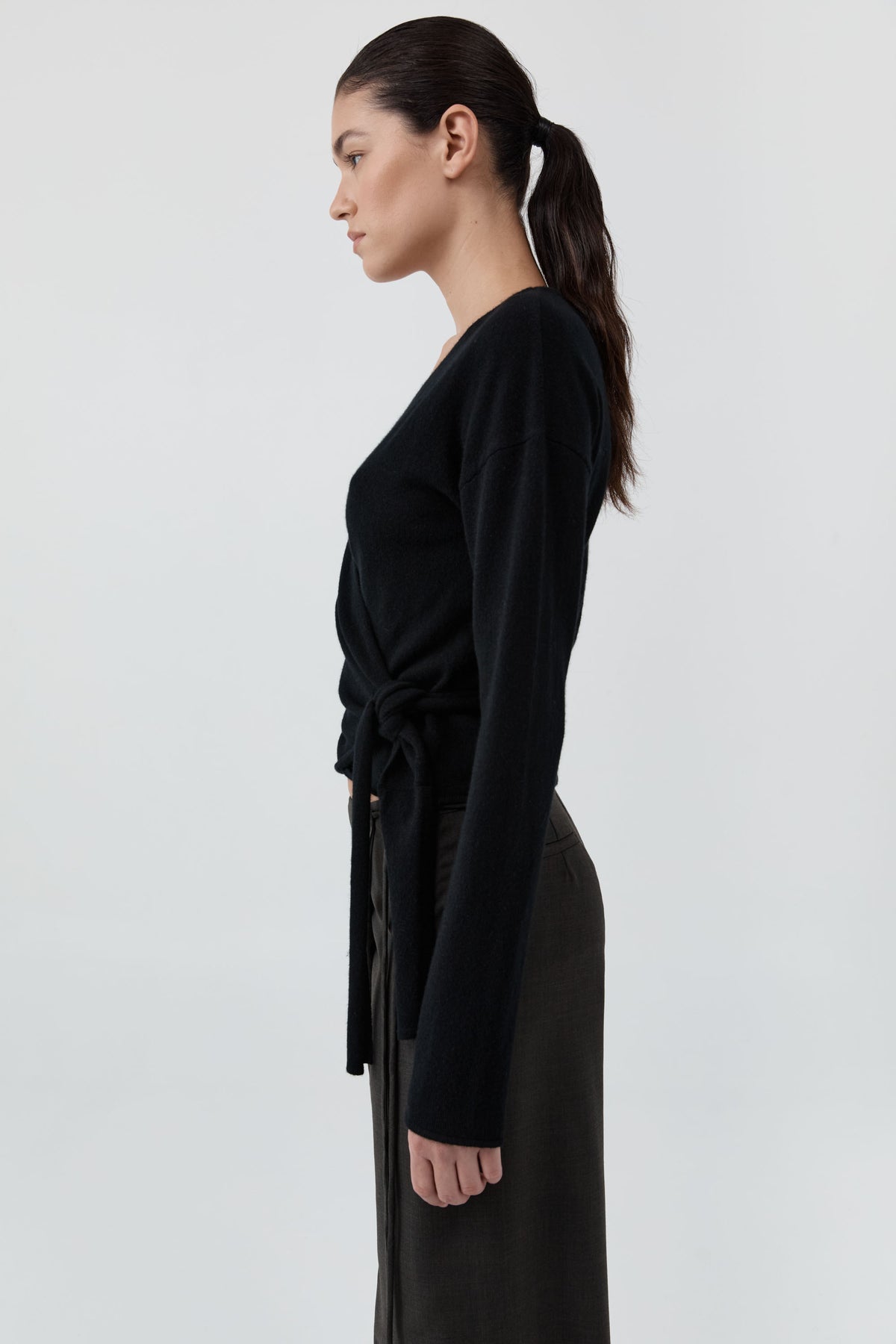 Side profile of a woman wearing St Agni Baby Wool Wrap Top and gray pants standing against a white background