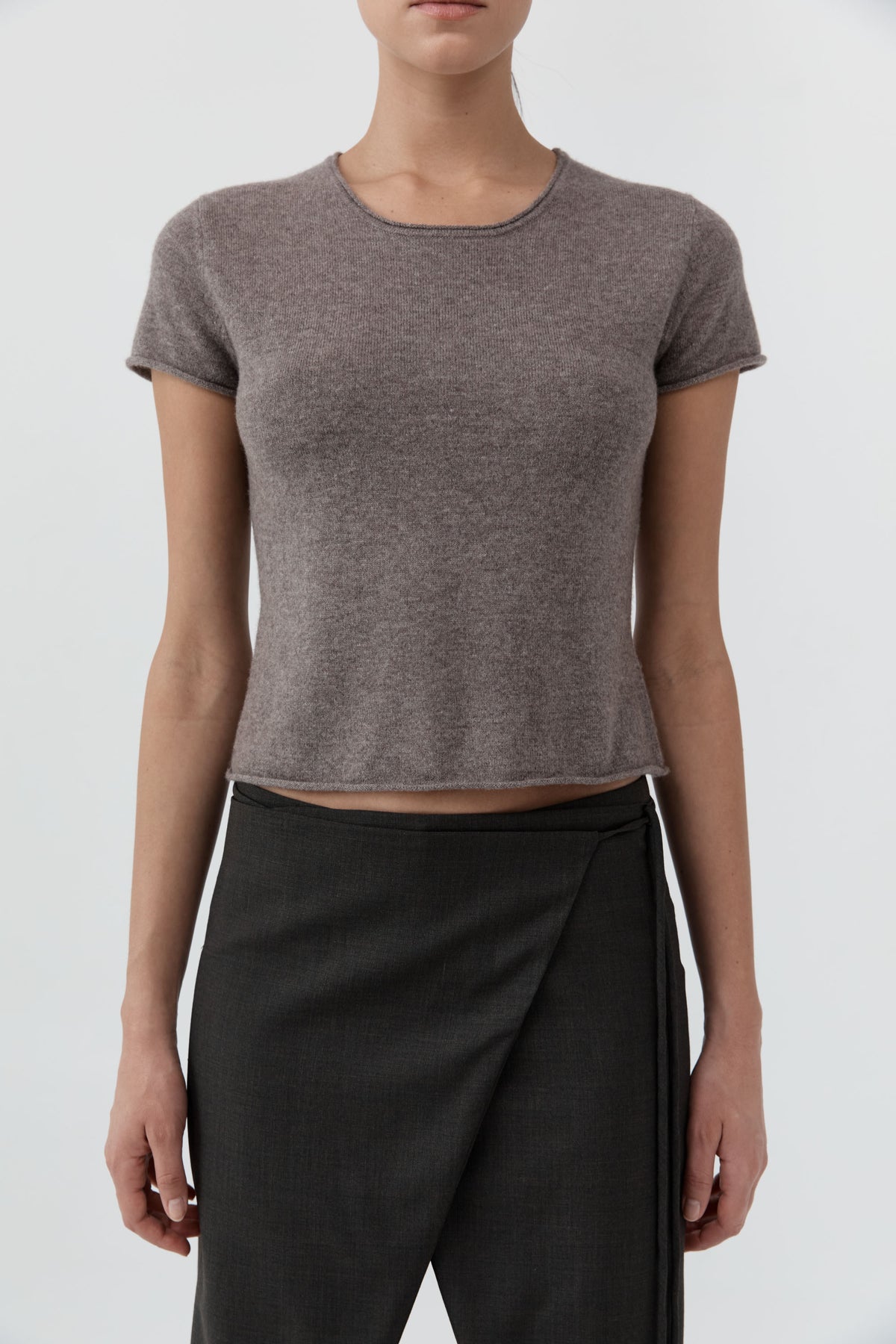 Close up of a woman wearing the St Agni Fine Merino Wool Baby Tee with black pants standing against a white background