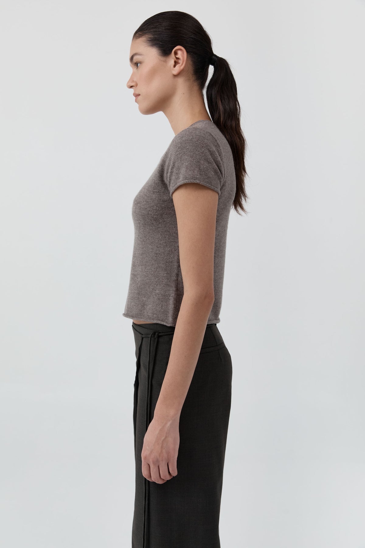 Side profile of woman wearing the St Agni Fine Merino Wool Baby Tee with black pants standing against a white background