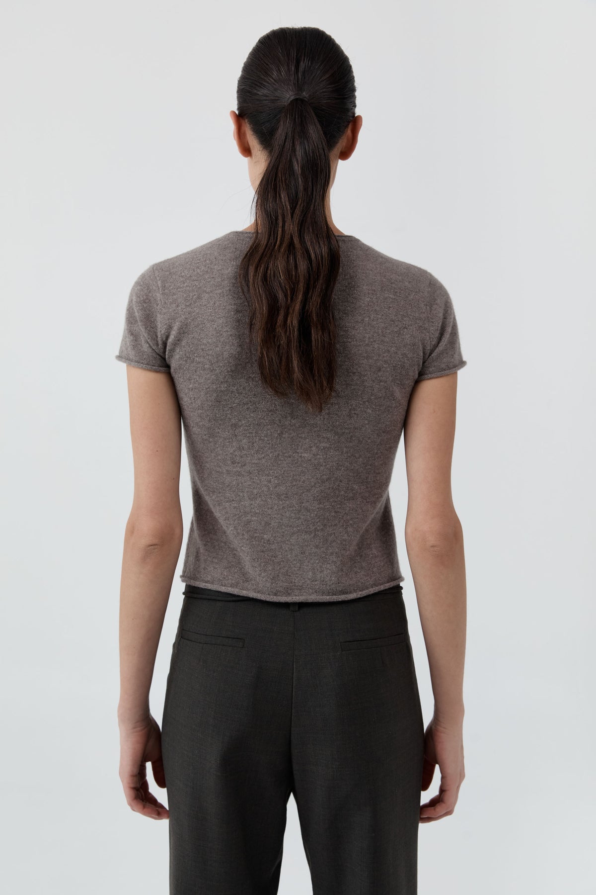 Backside of a woman wearing the St Agni Fine Merino Wool Baby Tee with black pants standing against a white background