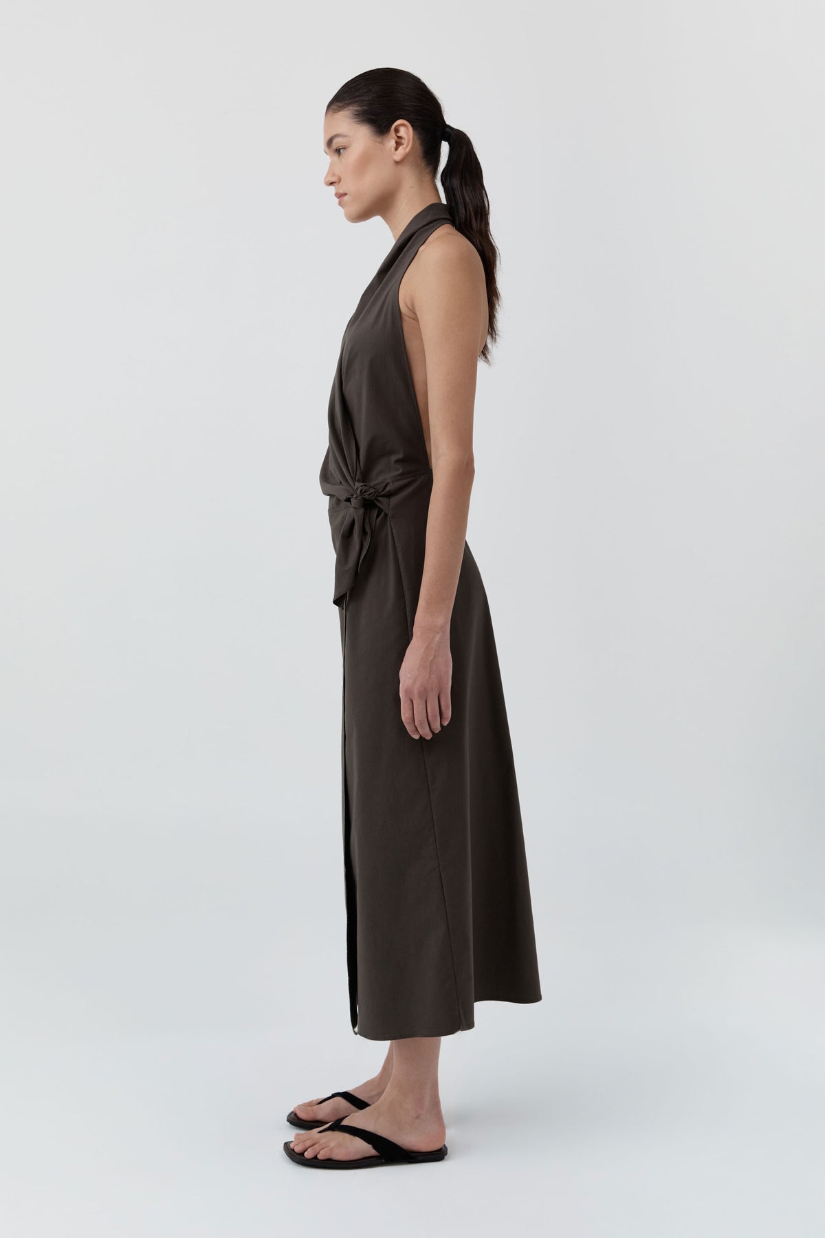 Side profile of a woman wearing St Agni Halter Wrap Backless Dress standing against a white background