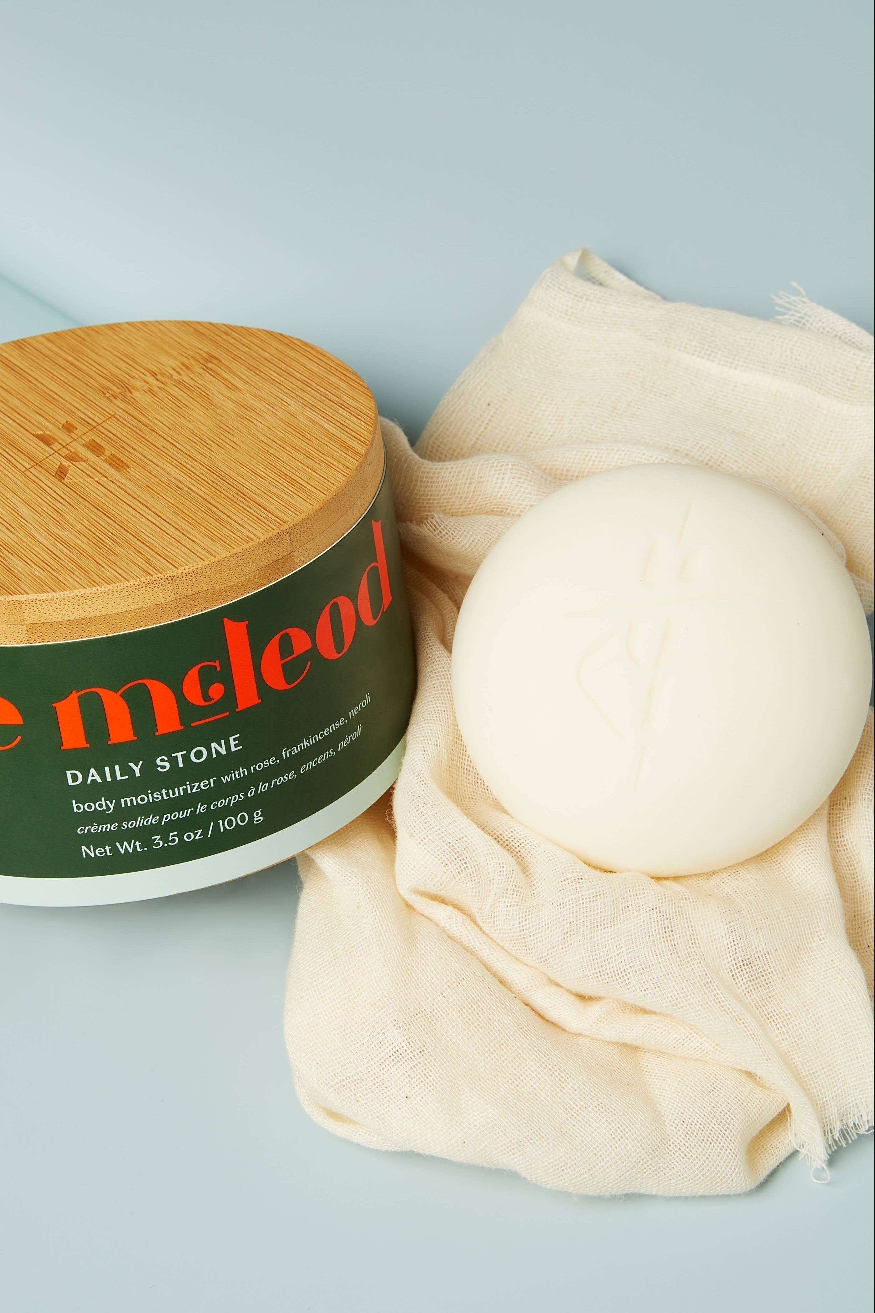 Jar of 'kate mcLeod' body moisturizer with a stone on a light blue background