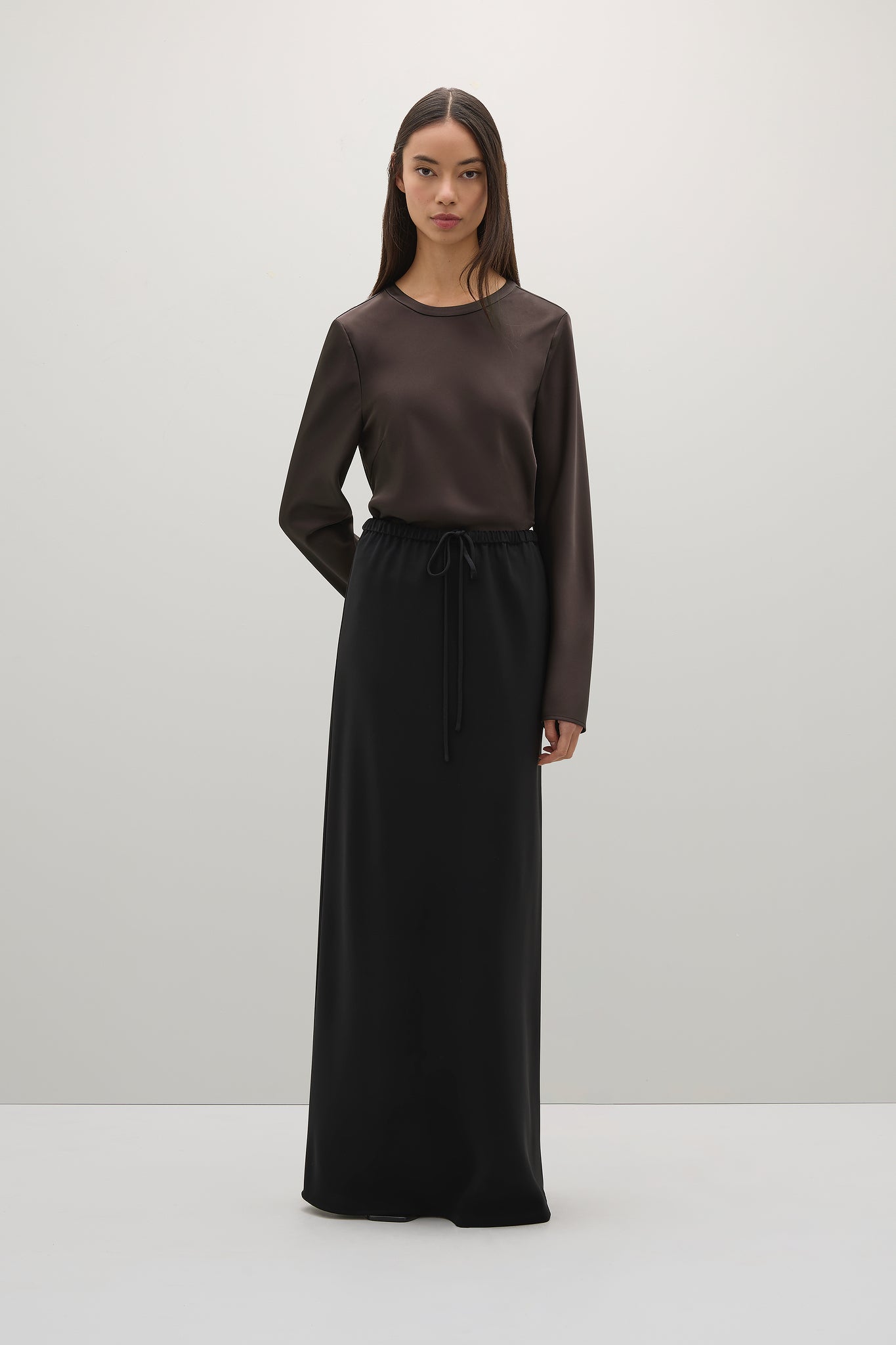Woman wearing a brown long-sleeve top and black skirt on a white background