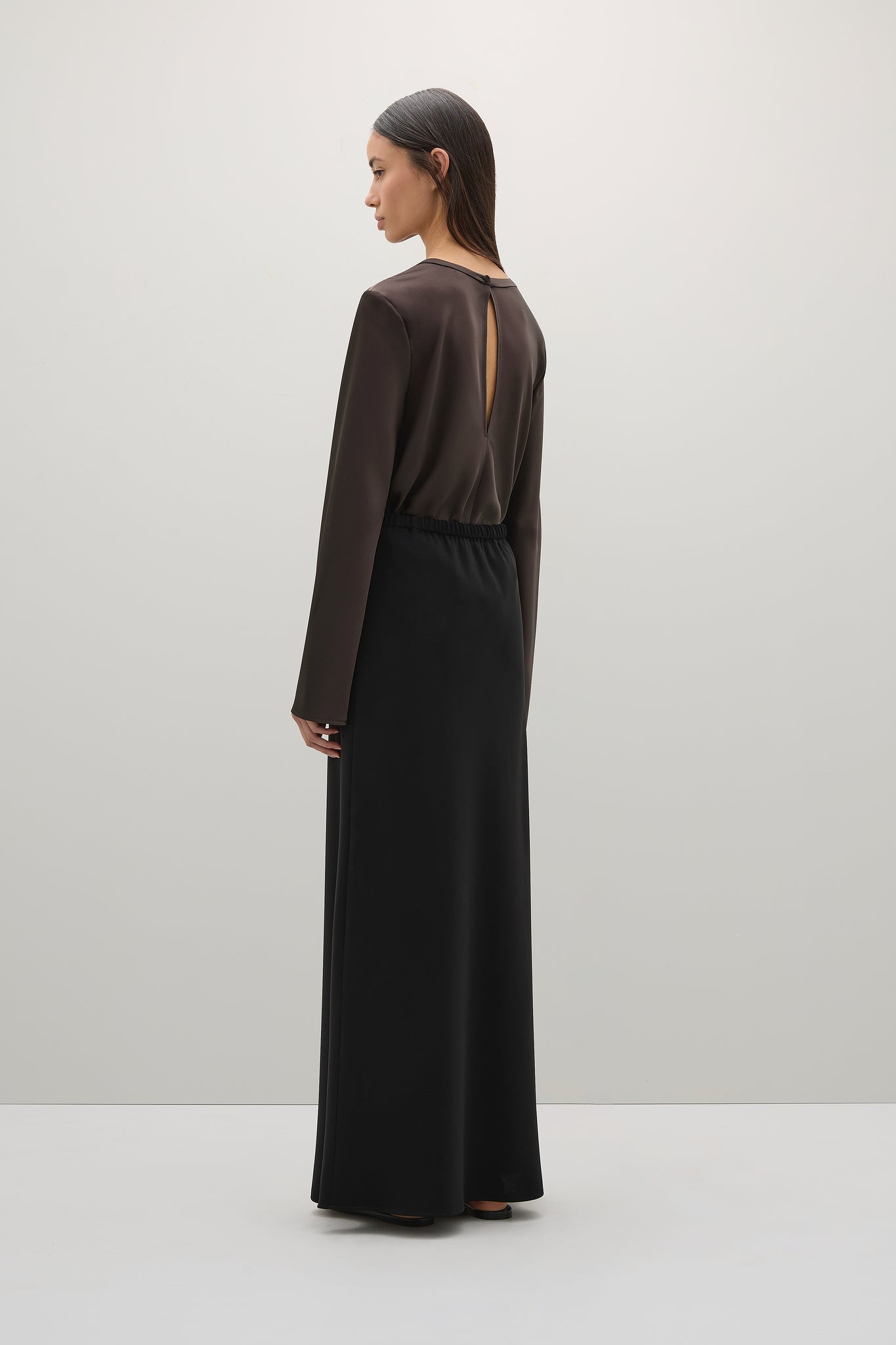 Woman wearing a long brown dress with a sheer back on a white background