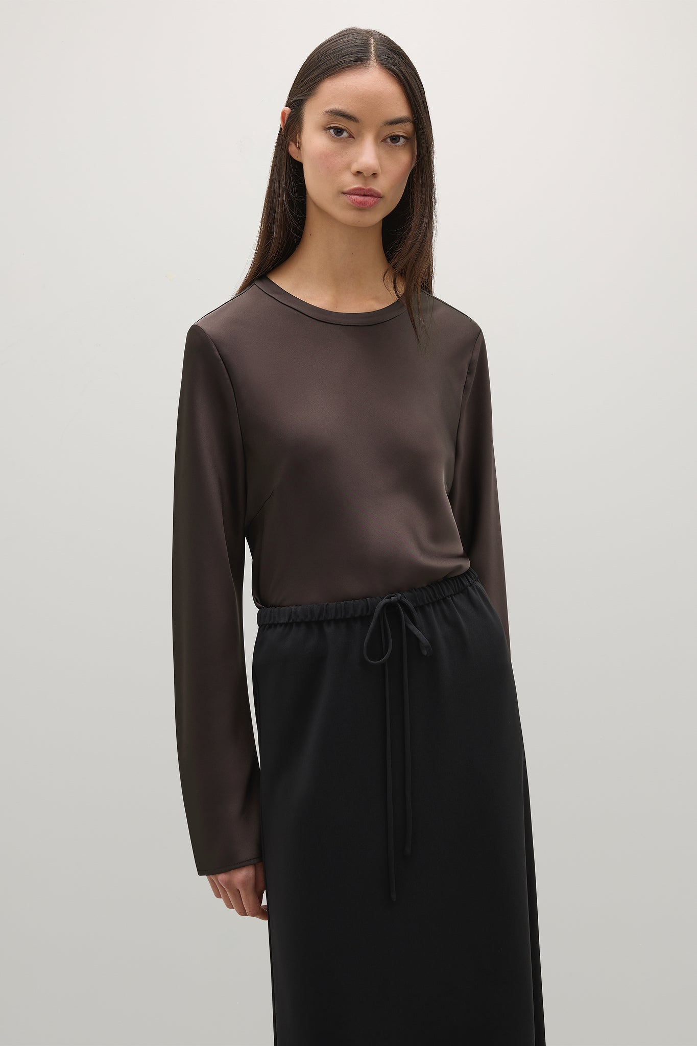 Woman wearing a brown long-sleeve top and black pants on a light gray background