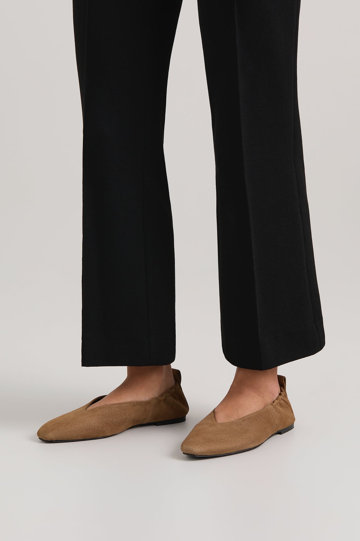 Person wearing black pants and tan shoes on a plain background
