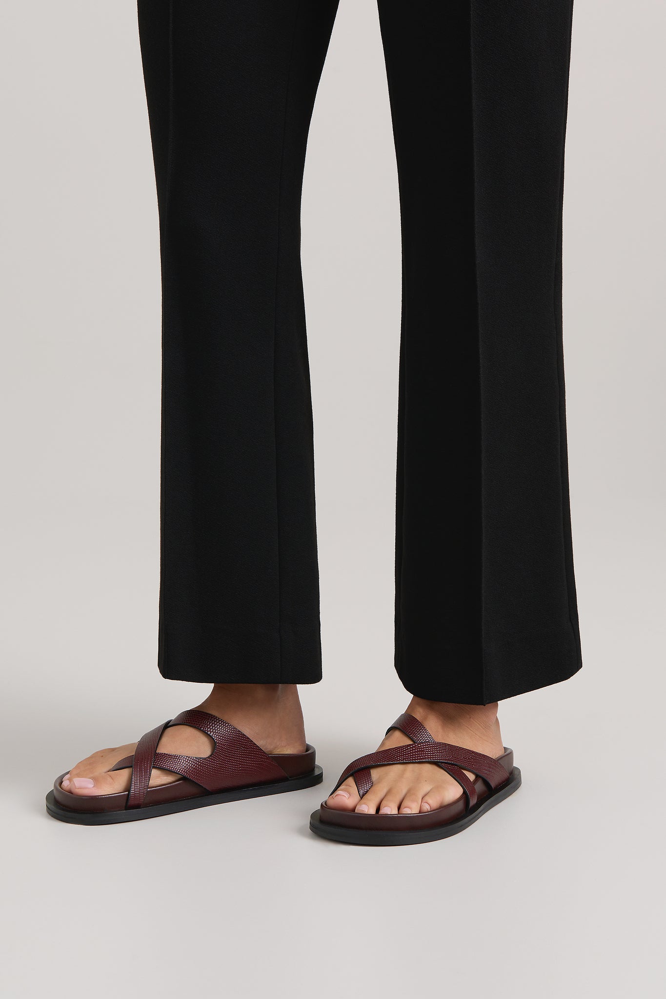 Person wearing dark brown sandals with black pants on a light gray background