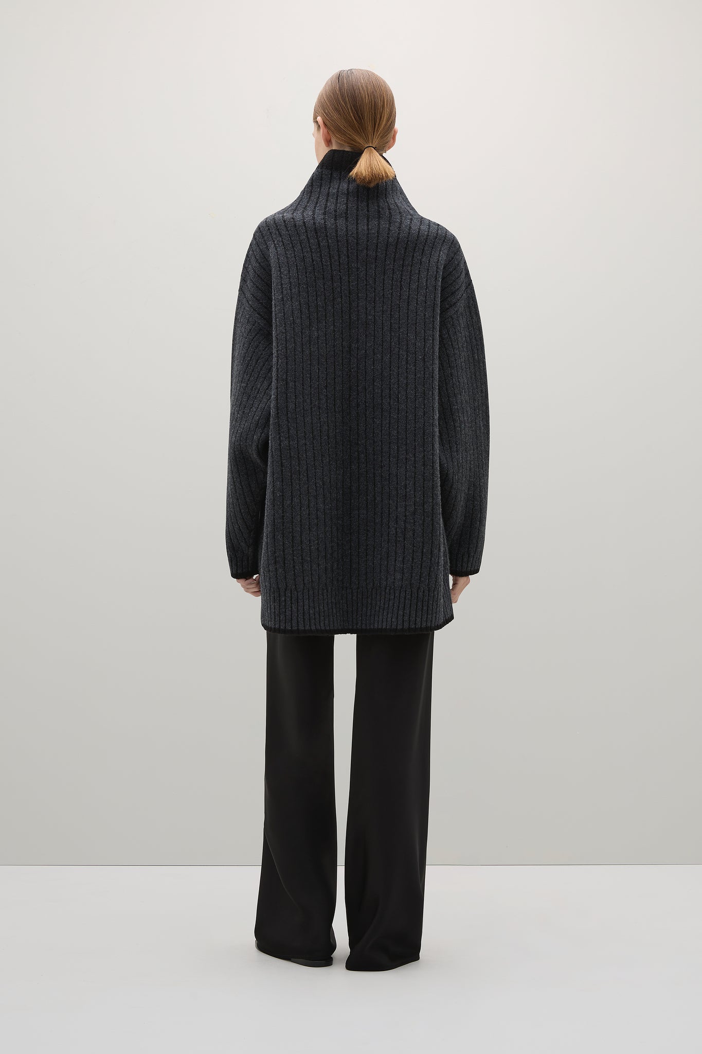Person wearing a dark gray ribbed sweater and black pants on a white background