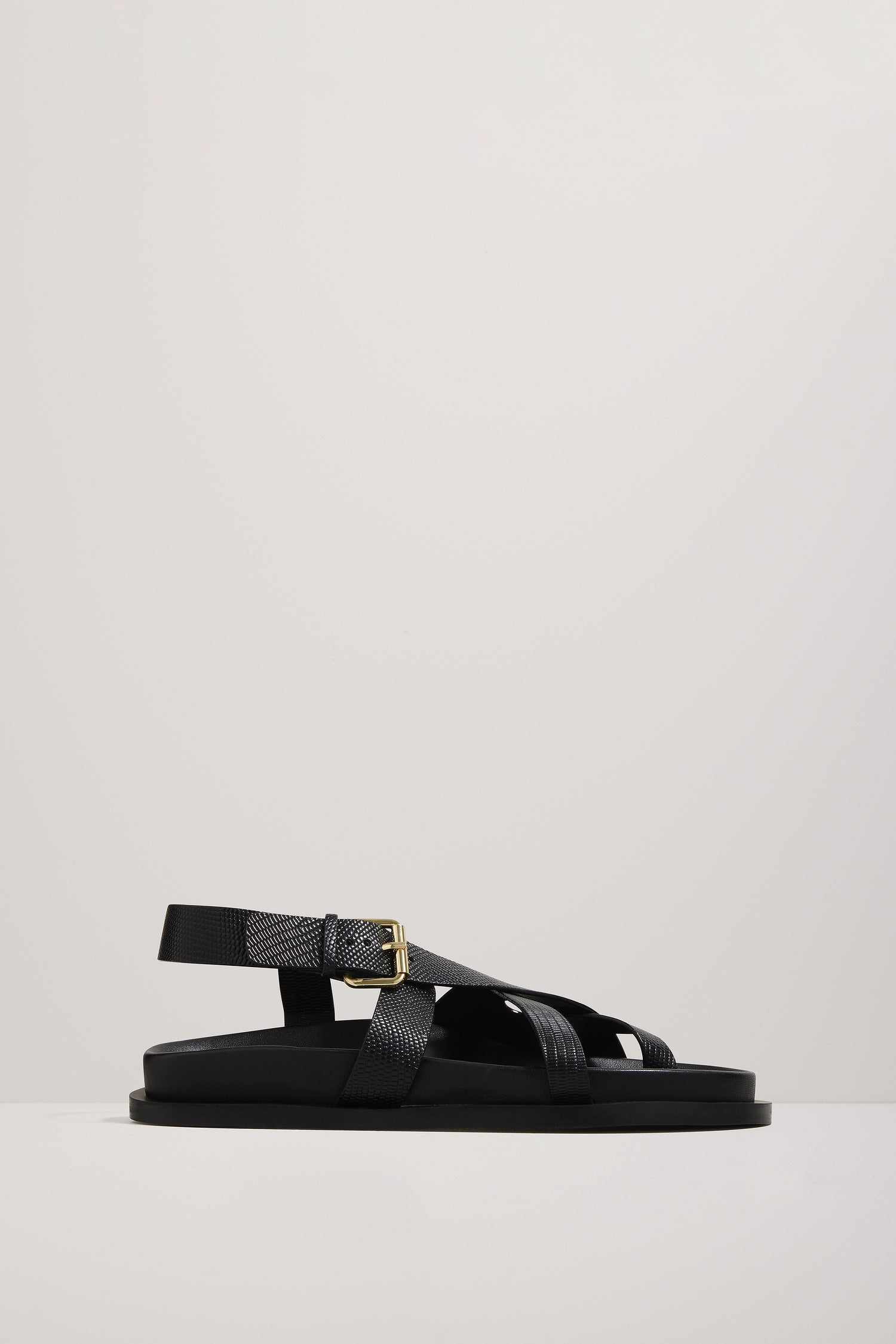 Black sandal with a gold buckle on a light gray background