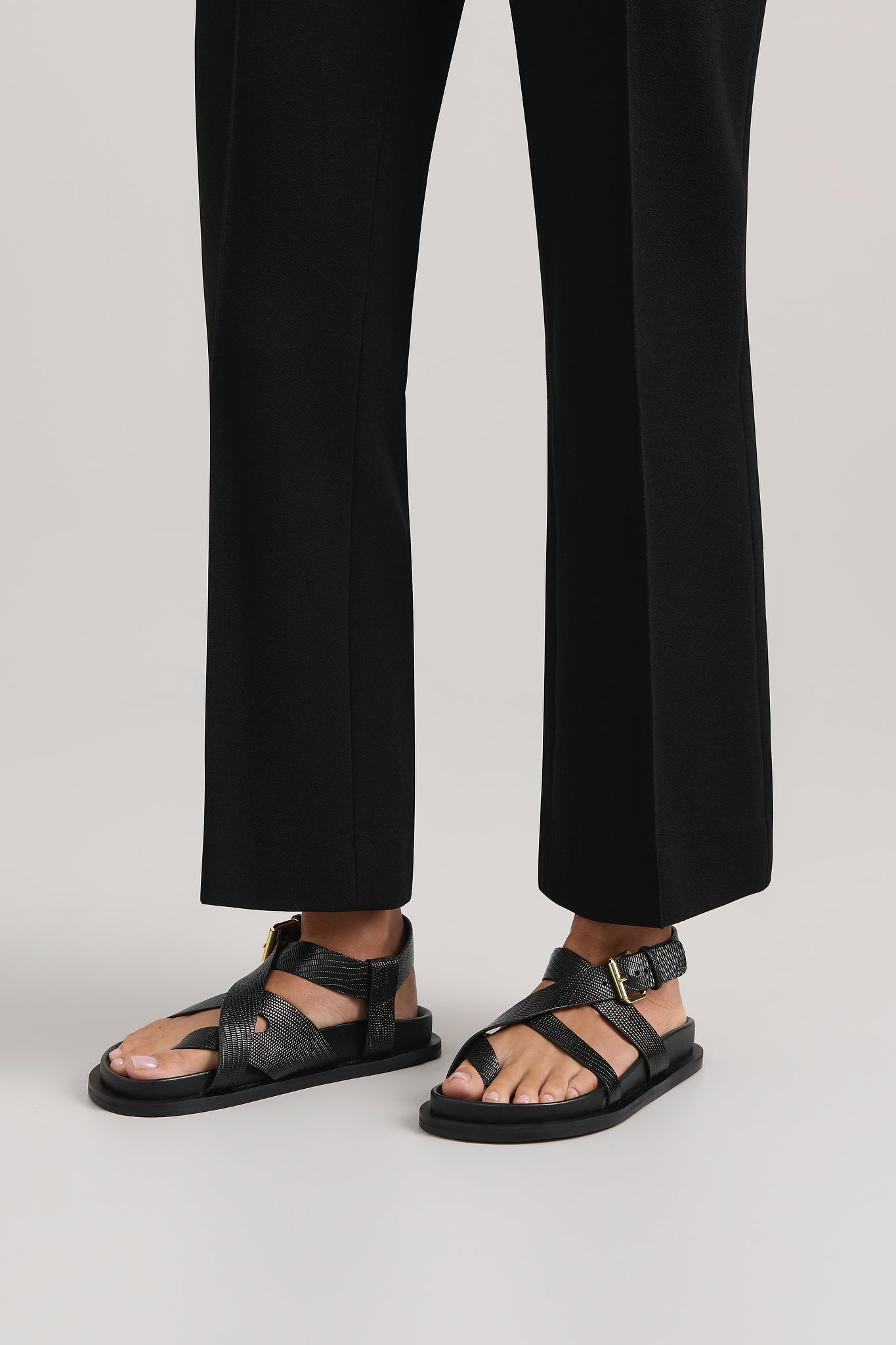 Person wearing black sandals and black pants on a light gray background