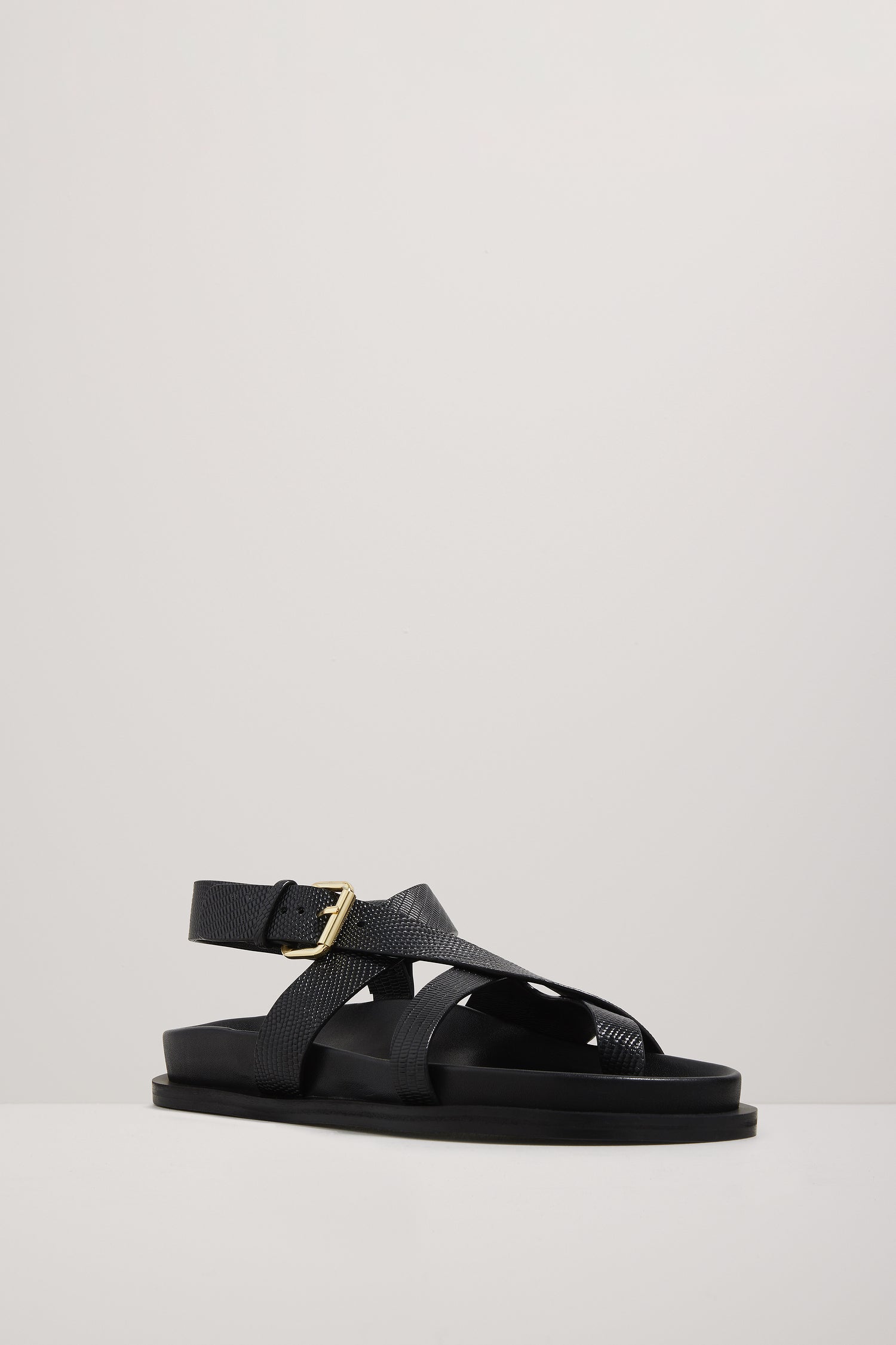 Black sandal with a gold buckle on a light gray background