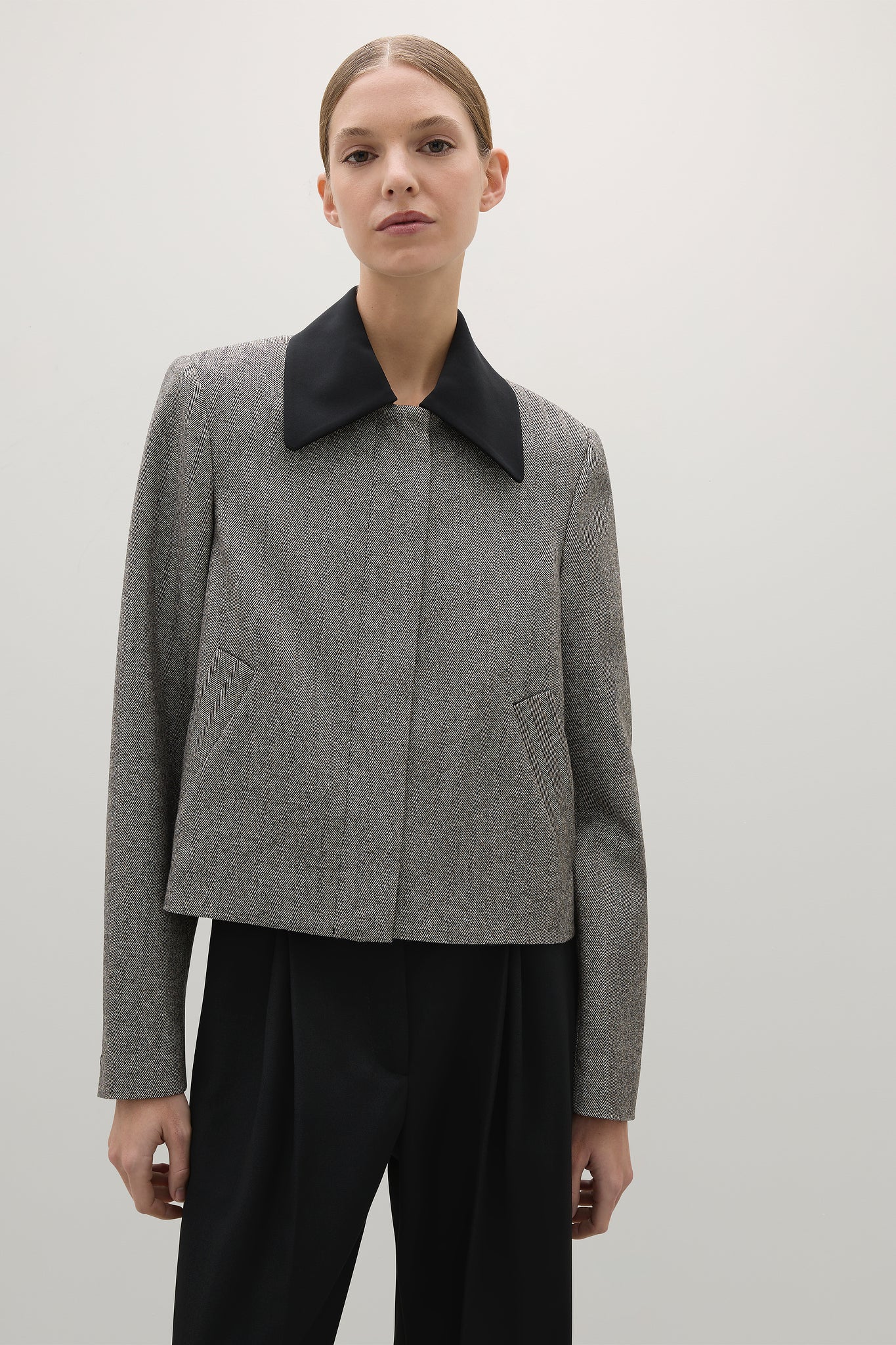 Person wearing a gray jacket with a black collar against a plain background