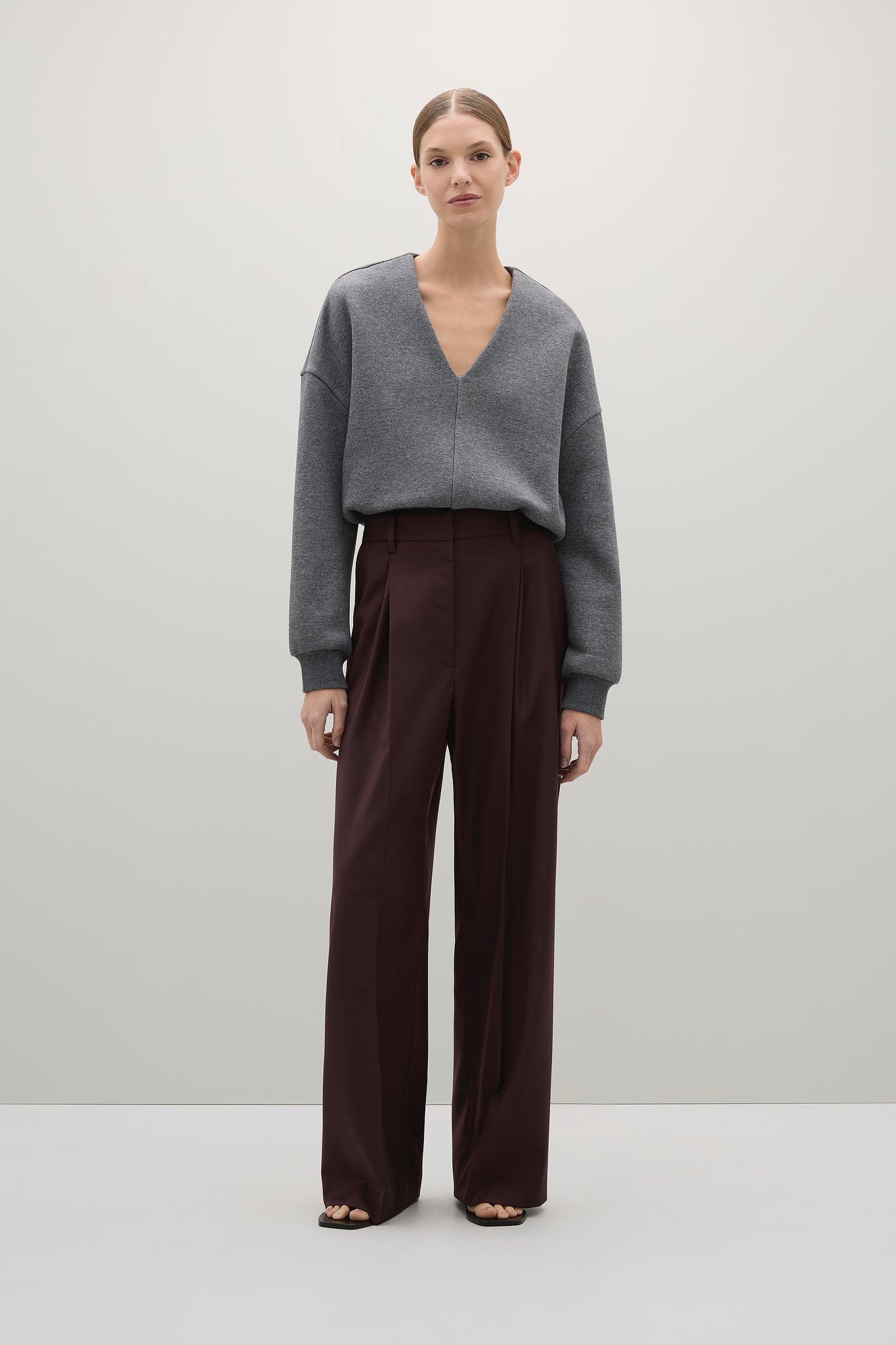 Woman wearing a gray sweater and dark brown pants on a white background