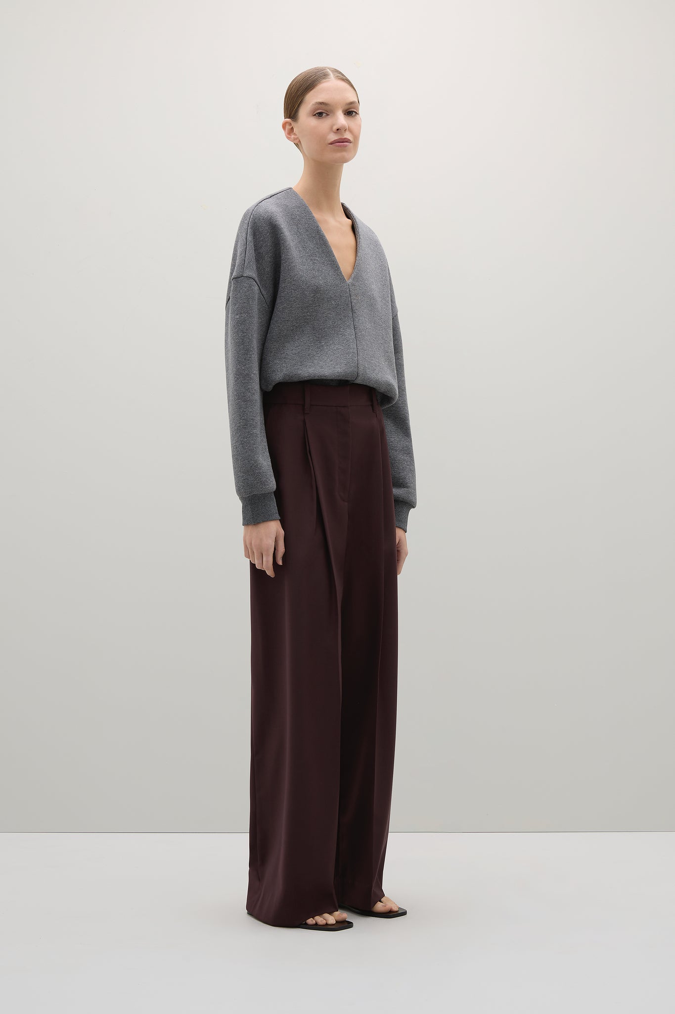 Woman wearing a gray sweater and dark brown pants on a white background