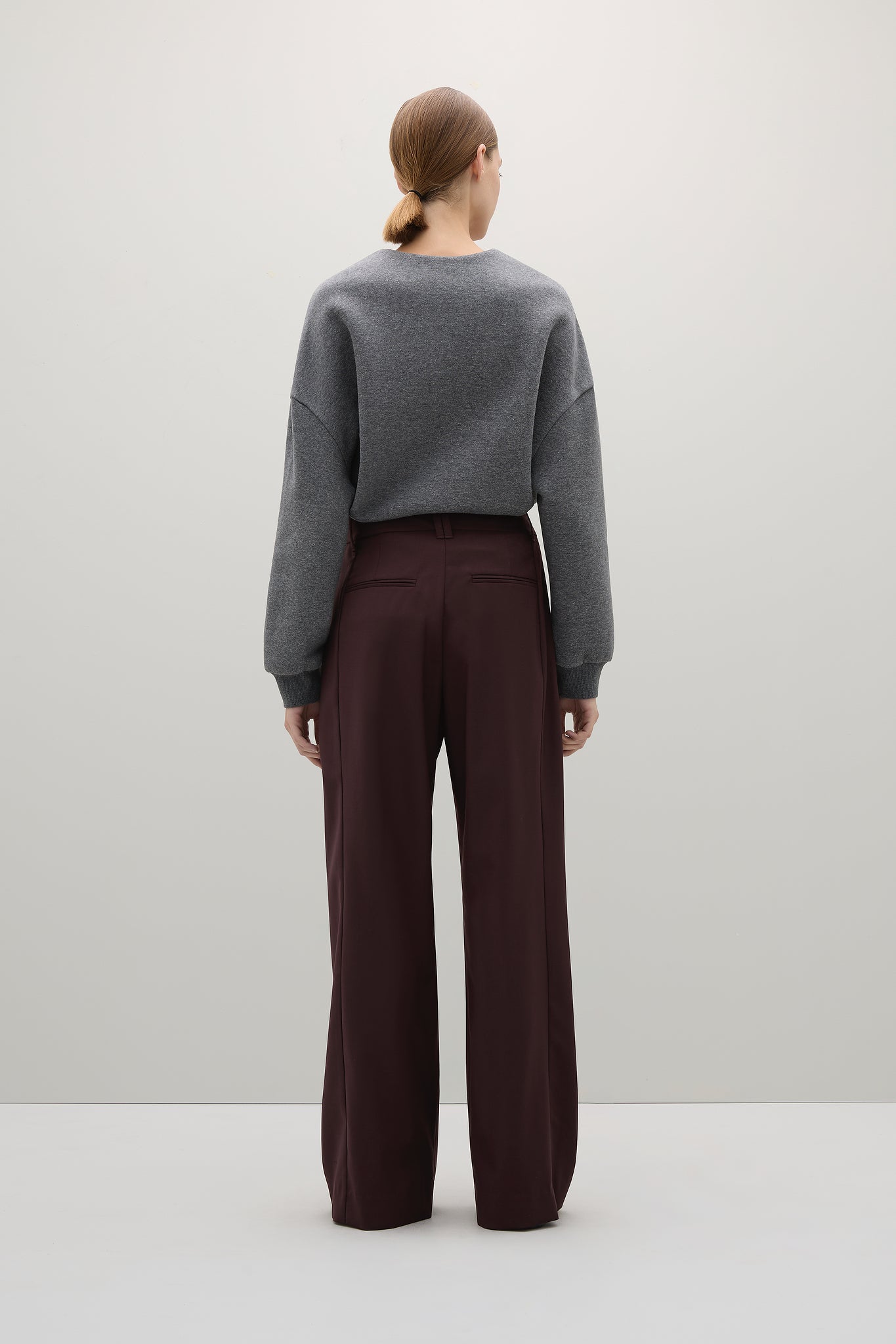 Person wearing a gray sweater and brown pants on a white background