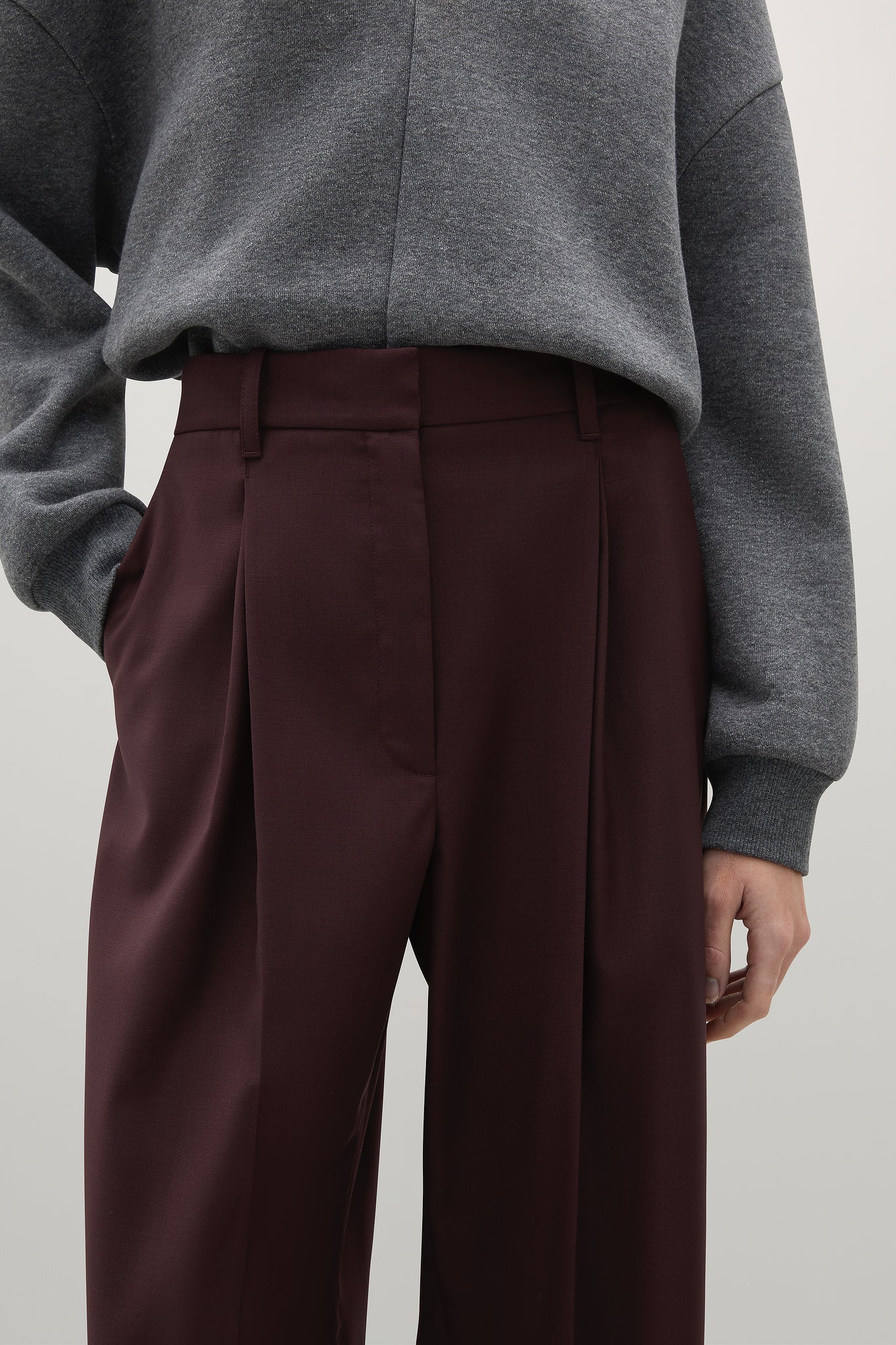 Person wearing a gray sweater and maroon pants on a plain background
