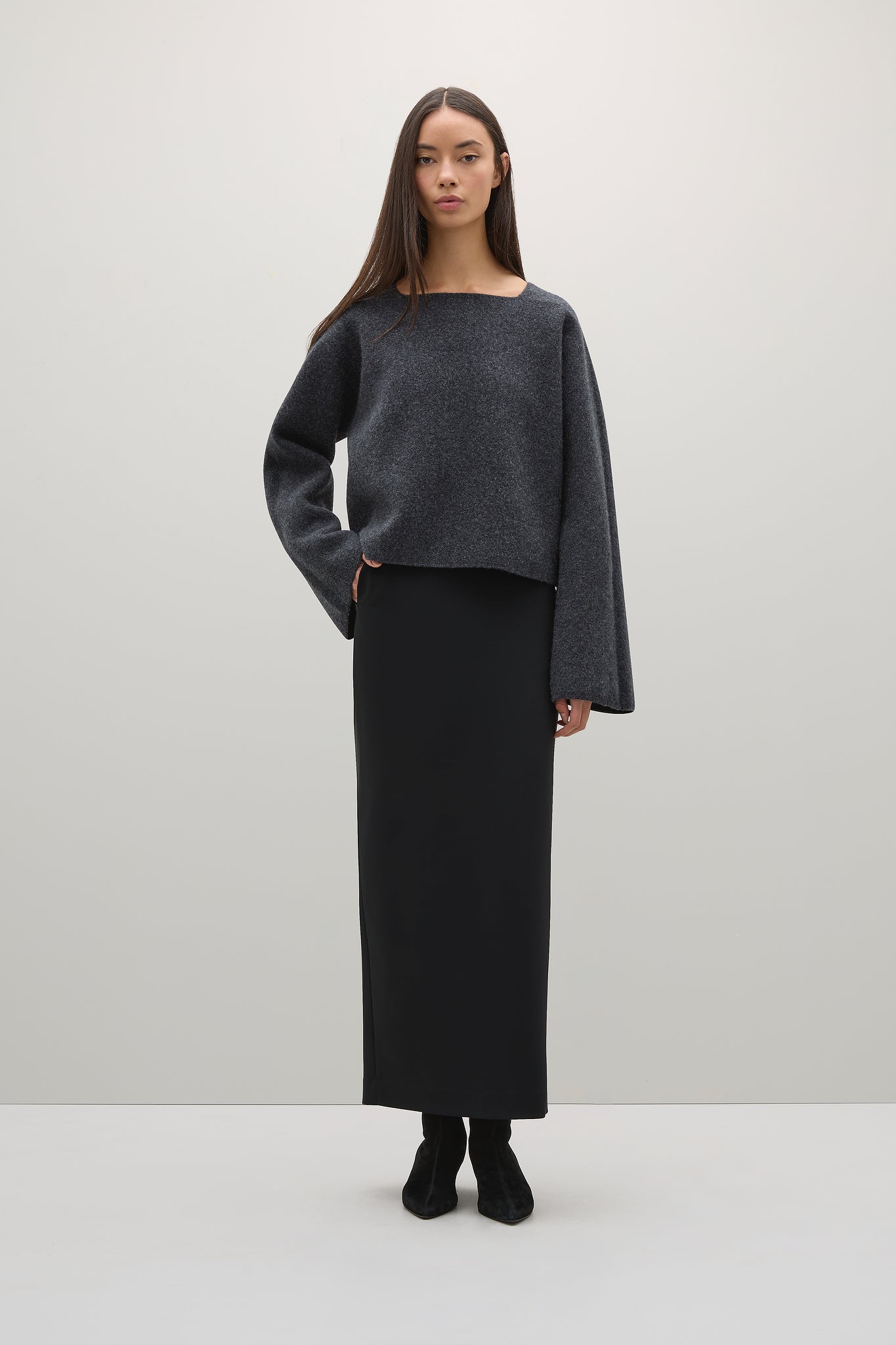 Woman wearing a dark gray sweater and black skirt on a white background