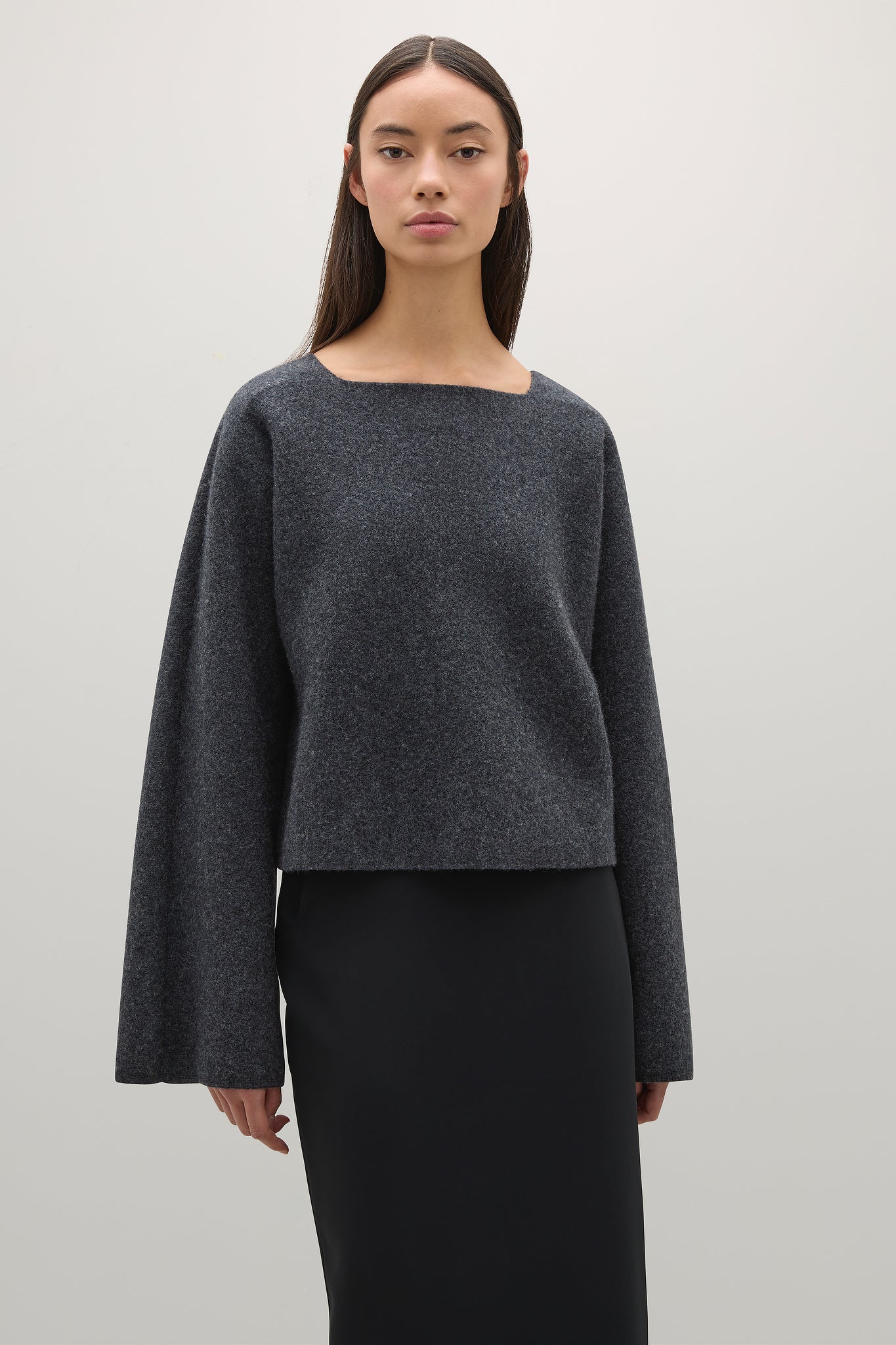 Woman wearing a dark gray sweater over a black dress on a light gray background